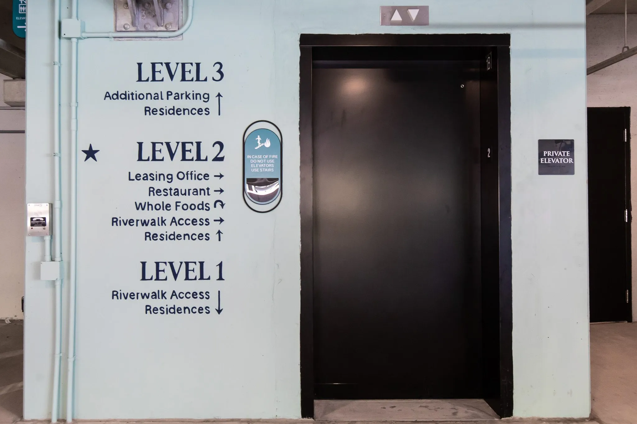 Multifamily parking garage elevator lobby with level directory signage beside a black elevator door