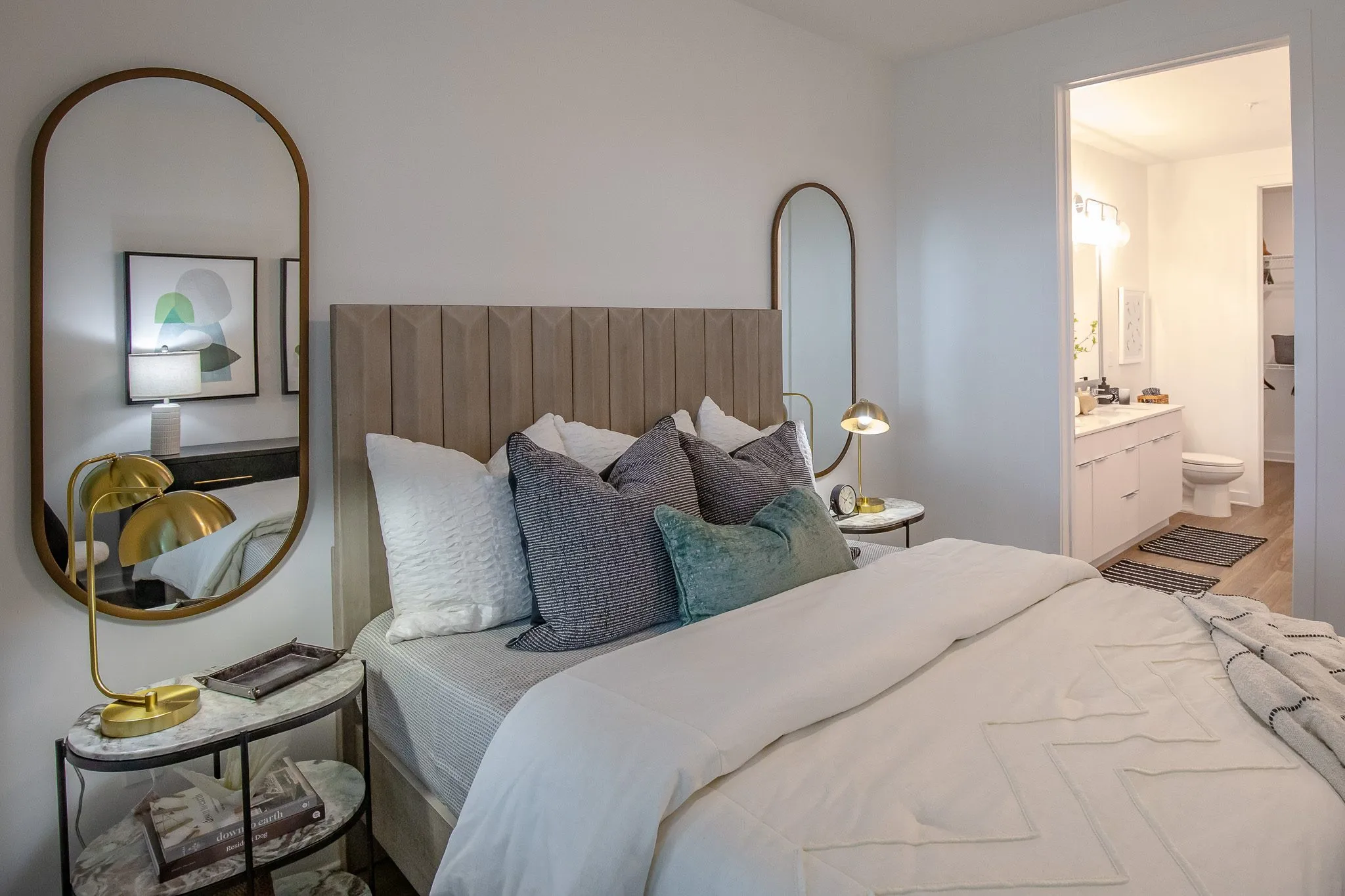 Multifamily model apartment bedroom with a channelled headboard, brass lamp on a marble nightstand and en suite bathroom