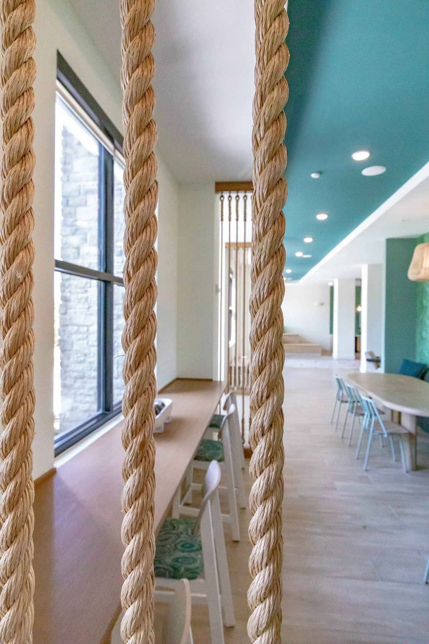Multifamily amenity banquette hall seen through thick rope strands, a window counter with stools