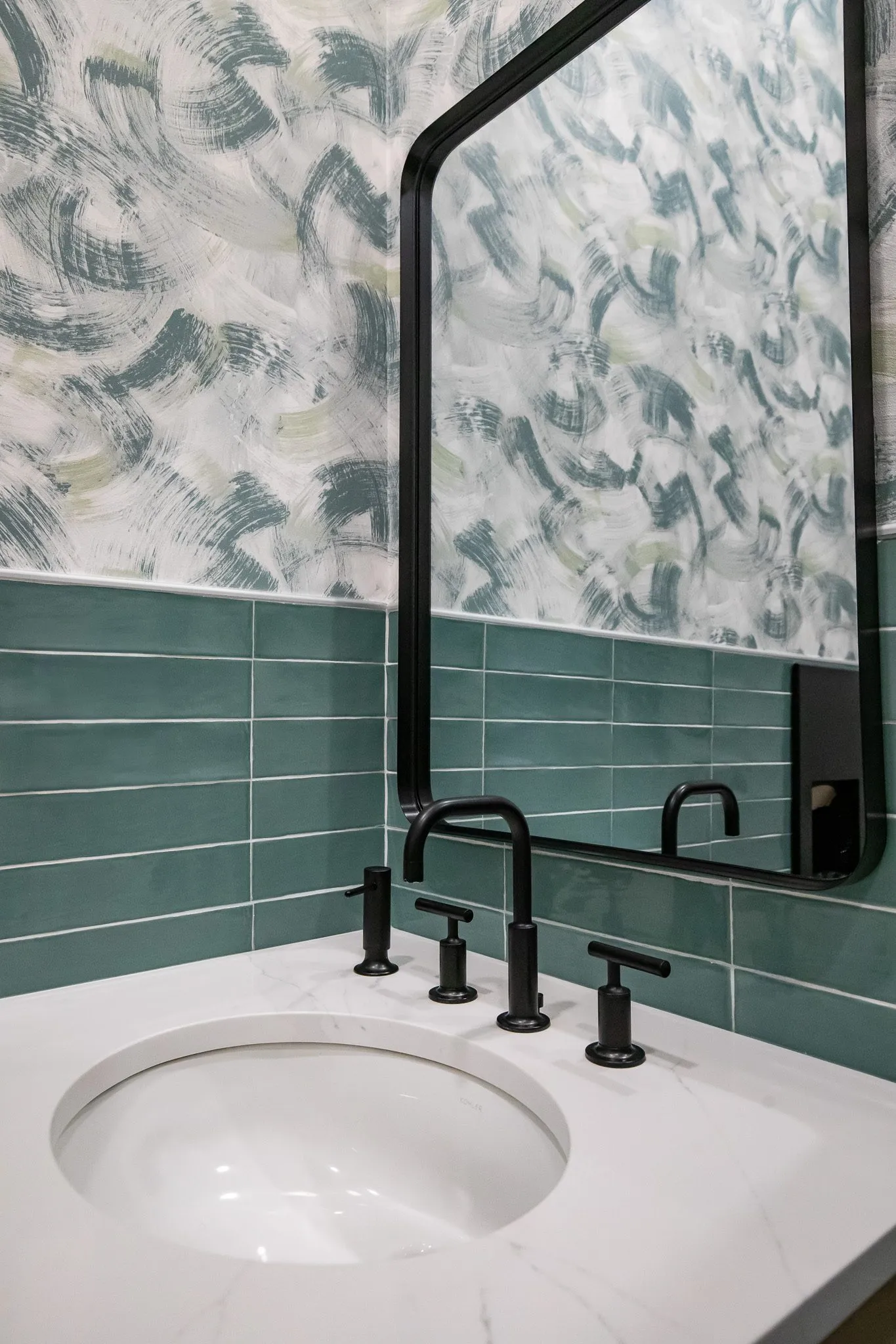 Multifamily interior detail: white undermount sink with a black faucet, green tile and brushstroke wallpaper, black mirror