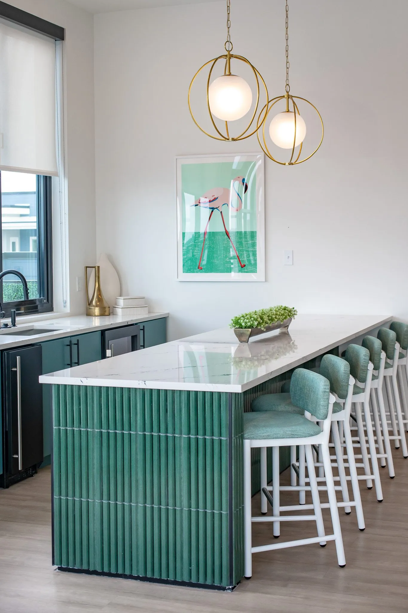 Multifamily kitchen island in fluted green tile with a row of green stools, a flamingo print on the wall