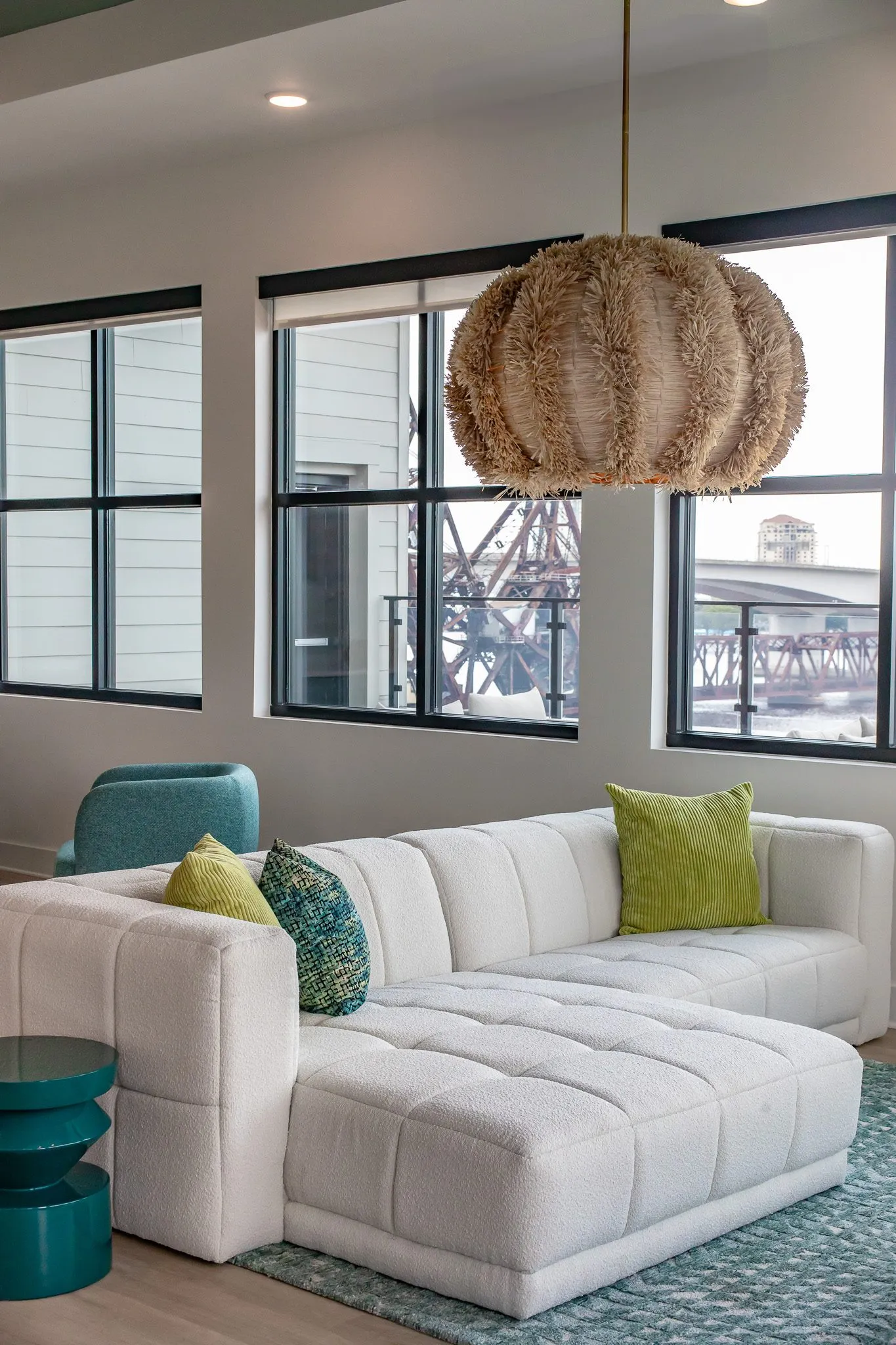 Multifamily interior detail: white sectional's chaise end with lime pillows under a rattan pendant by the windows