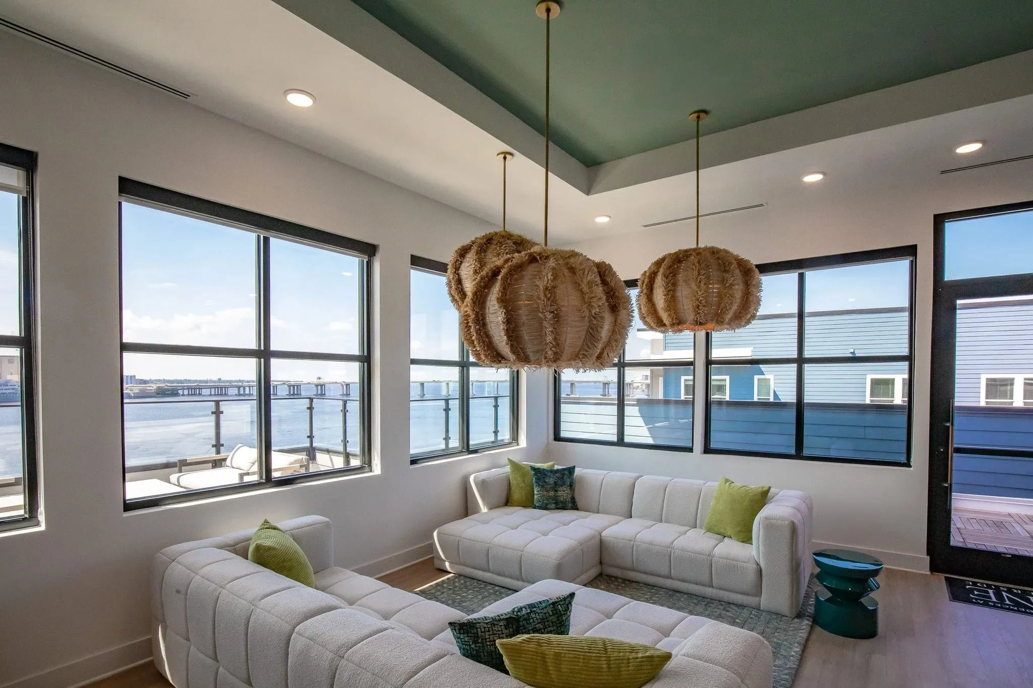 Multifamily amenity clubroom with a white sectional below woven pendants and a green ceiling, the St. Johns River outside