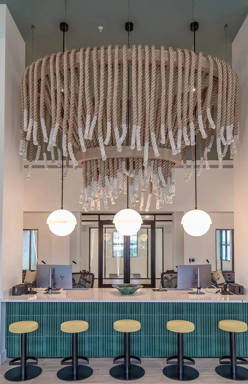 Multifamily leasing desk in fluted teal tile under a draped rope chandelier, interior design by Banko Design at One Riverside, Jacksonville, Florida
