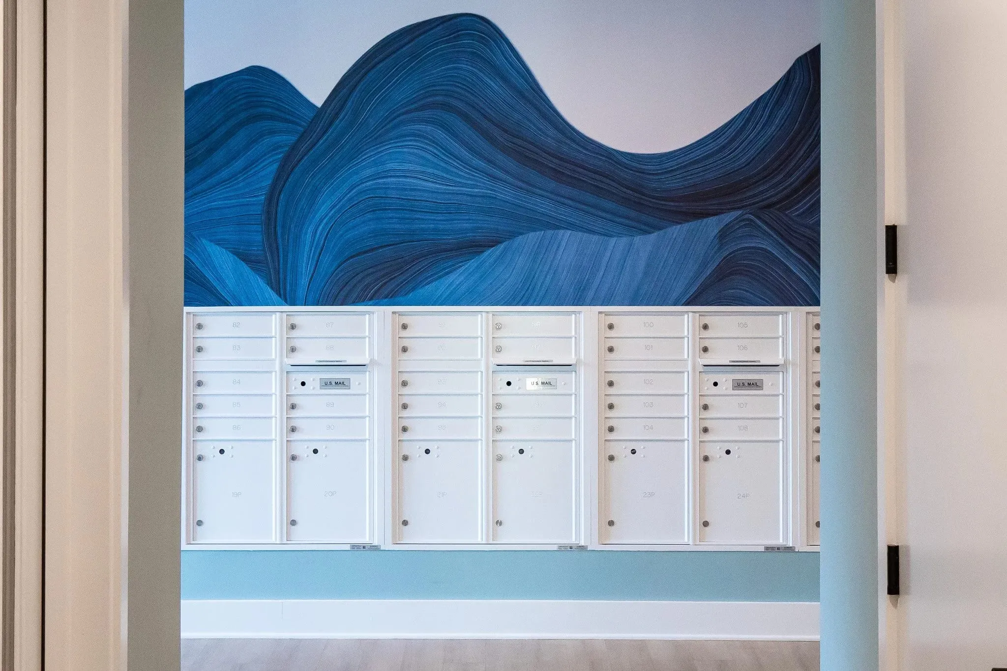 Multifamily amenity mail room with white mailboxes below a painted blue wave mural