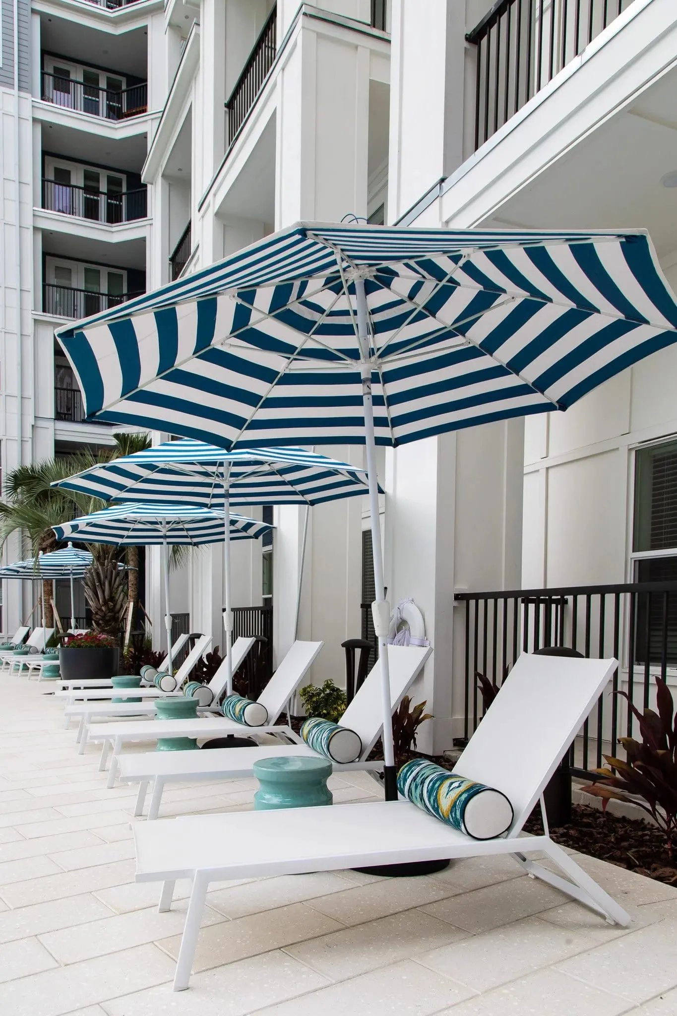 Multifamily amenity pool deck with a striped umbrella and loungers along the terrace