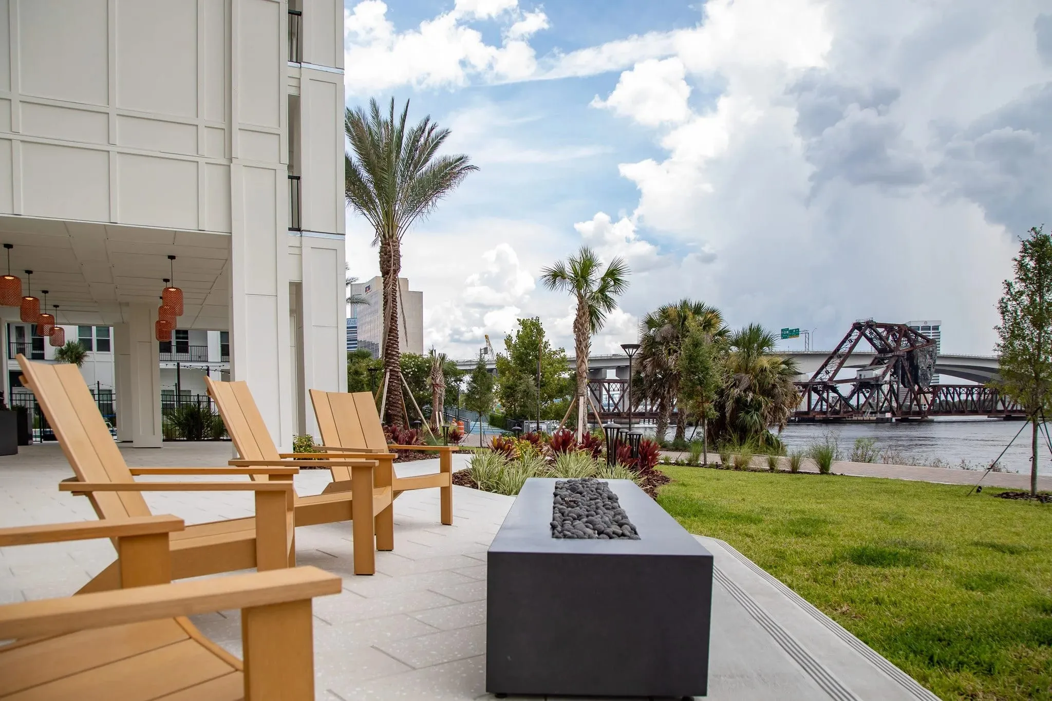 Multifamily amenity riverwalk lawn with Adirondack chairs and a firepit facing the lift bridge over the St. Johns River