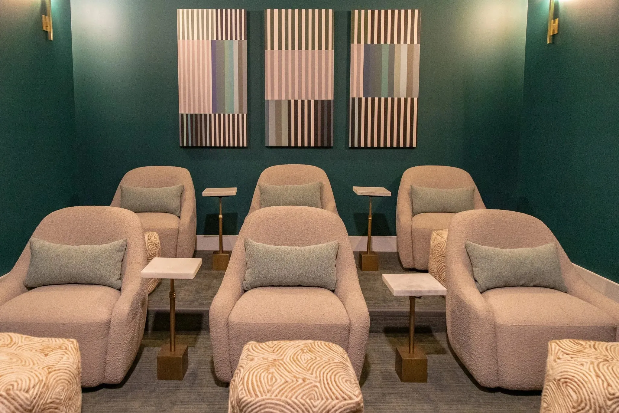 Multifamily amenity theater with rows of blush boucle armchairs and side tables, three striped prints on a deep green wall