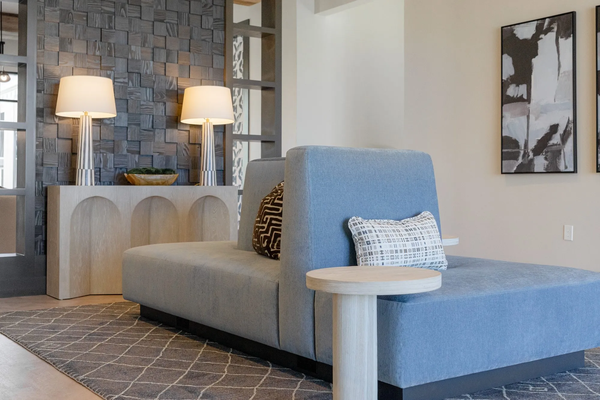 Multifamily interior detail: blue upholstered settee and round side table before an arched pale wood console, abstract print