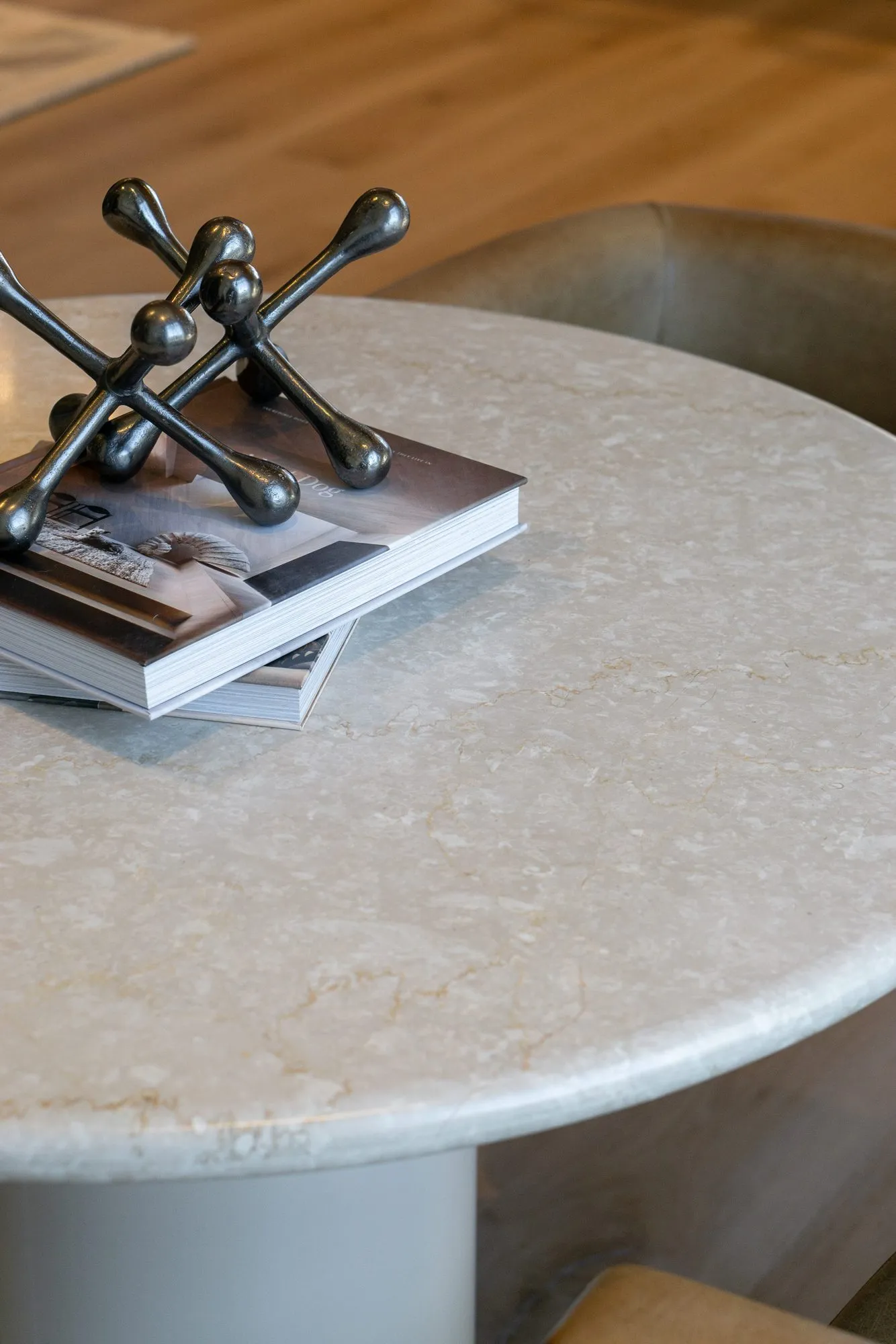 Multifamily interior detail: pale stone round table with books and a black metal jack sculpture