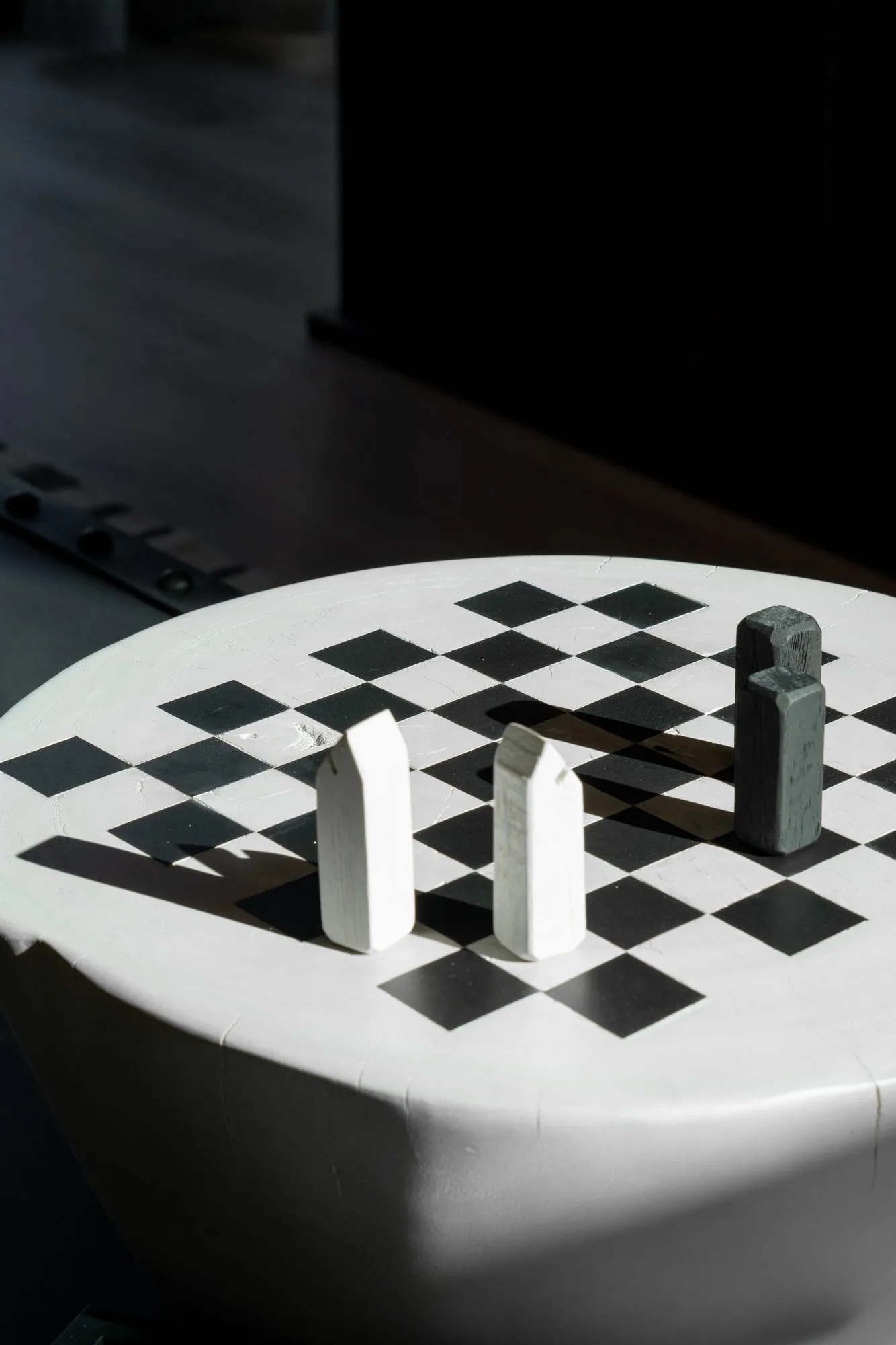 Multifamily interior detail: white drum table with a checkerboard top and black and white game pieces in shadow