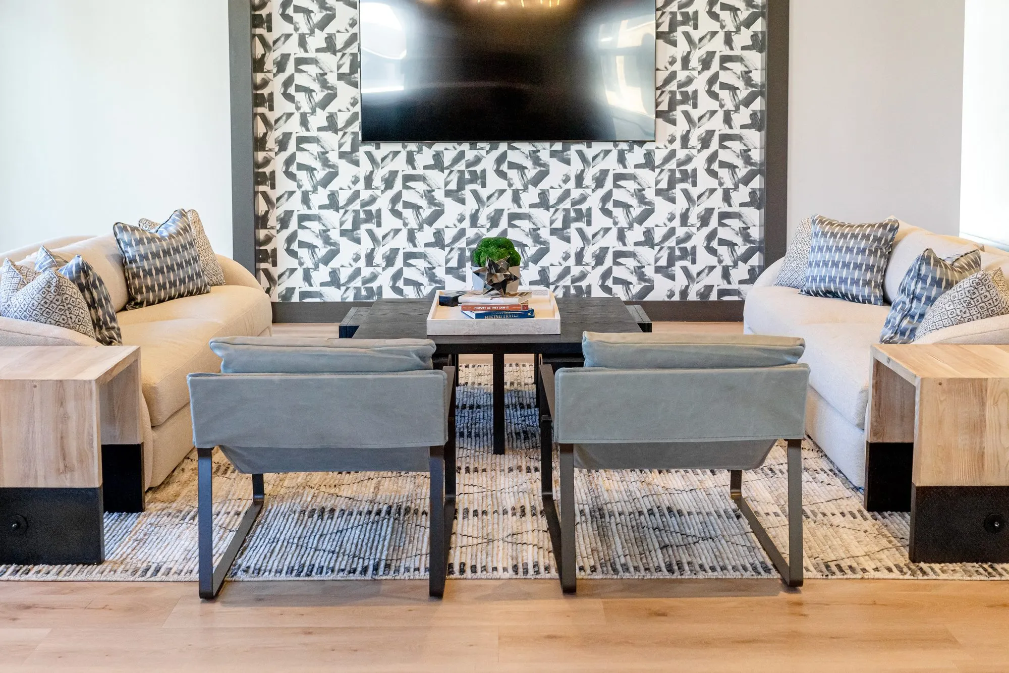 Multifamily amenity lounge with two cream sofas and grey sling chairs facing a TV on a black and white patterned tile wall