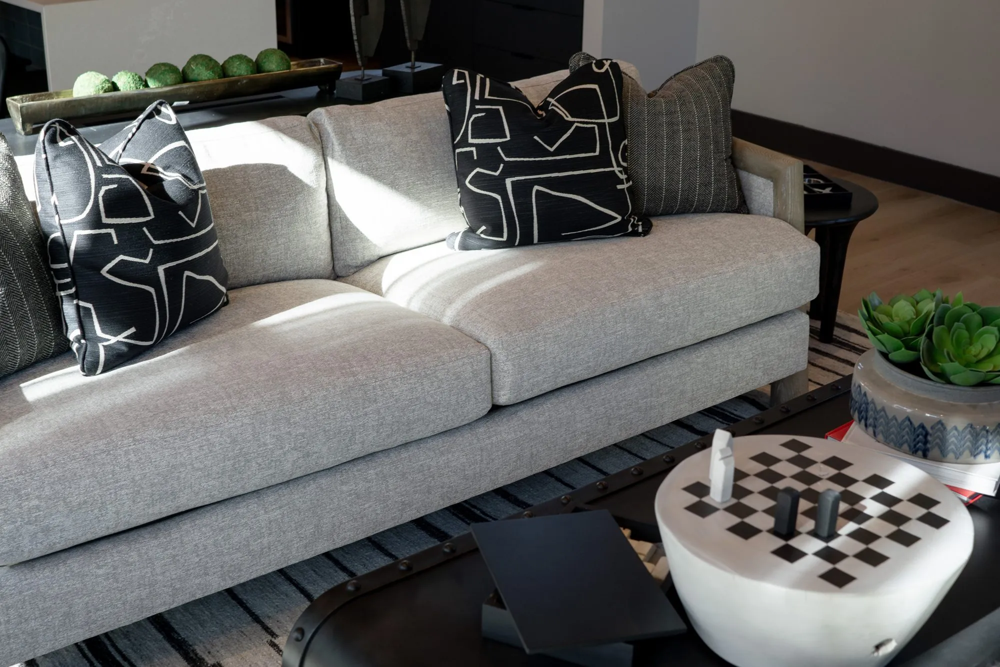 Multifamily interior detail: grey sofa with black and white graphic pillows beside a checkerboard drum table and succulents