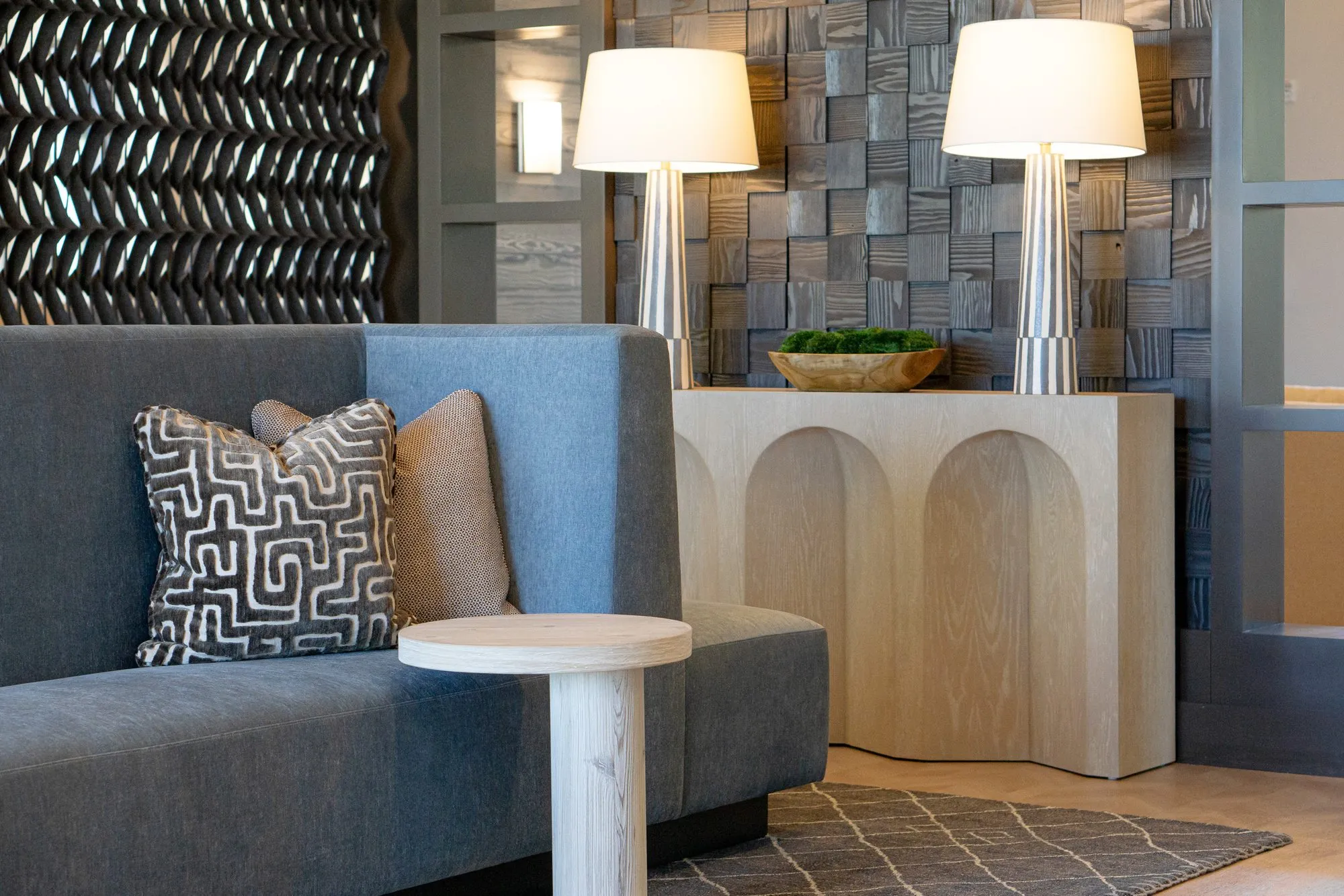 Multifamily interior detail: blue settee with a maze pattern pillow, twin lamps on the arched console and a carved block wall