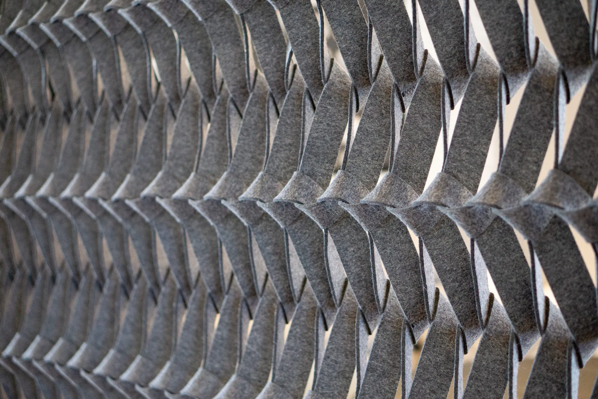 Multifamily interior detail: grey felt acoustic panel woven in an interlocking pattern, lit from the side