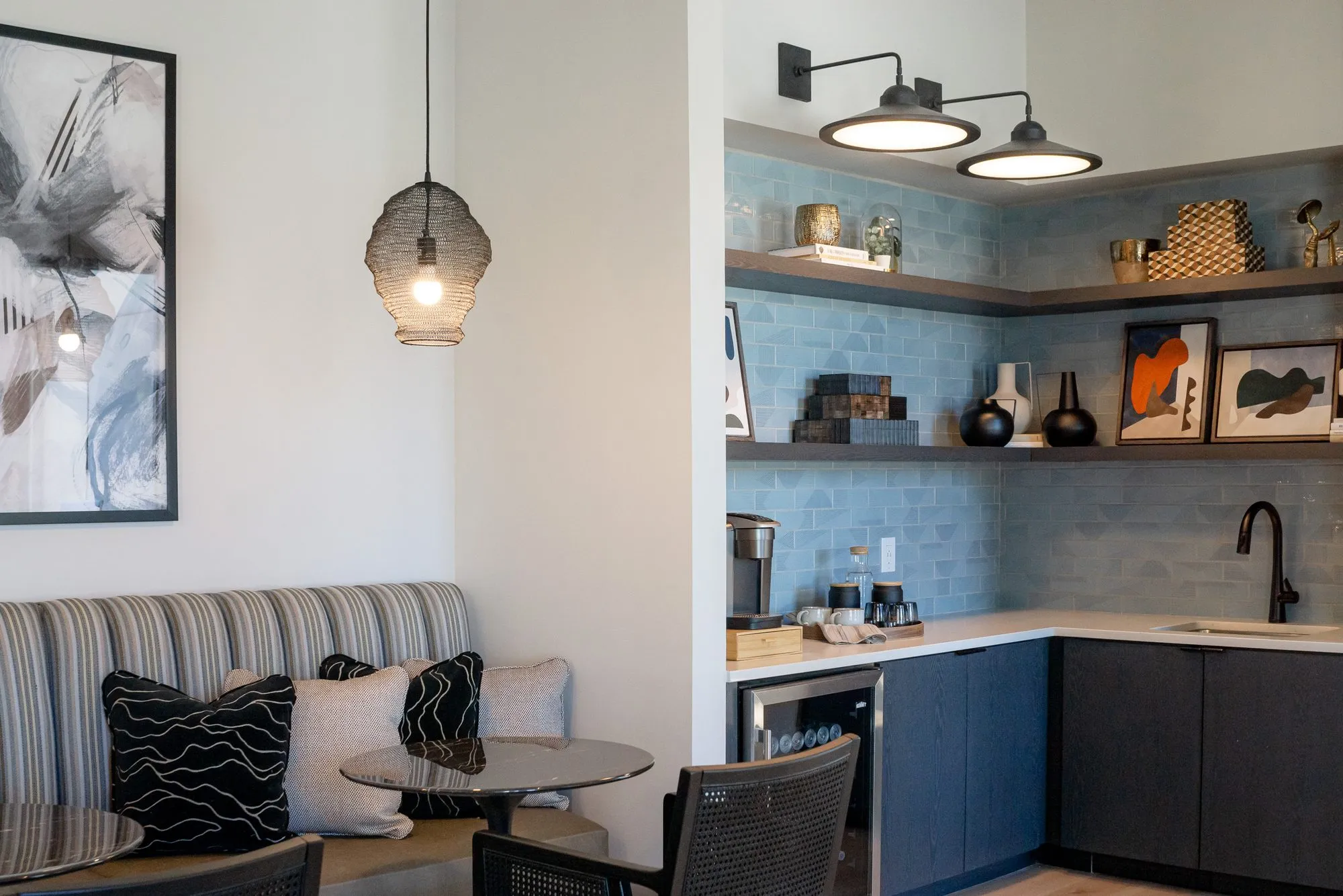 Multifamily amenity banquette corner with striped upholstery and a woven pendant beside a coffee bar with blue tile