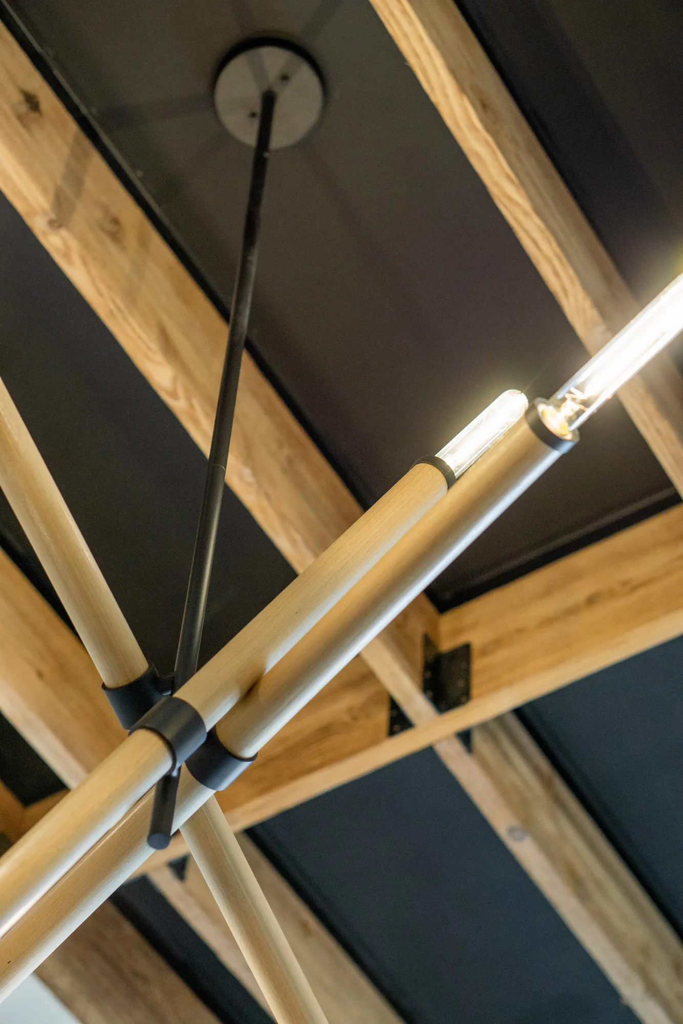 Multifamily interior detail: looking up at a linear brass and glass light fixture against exposed timber trusses