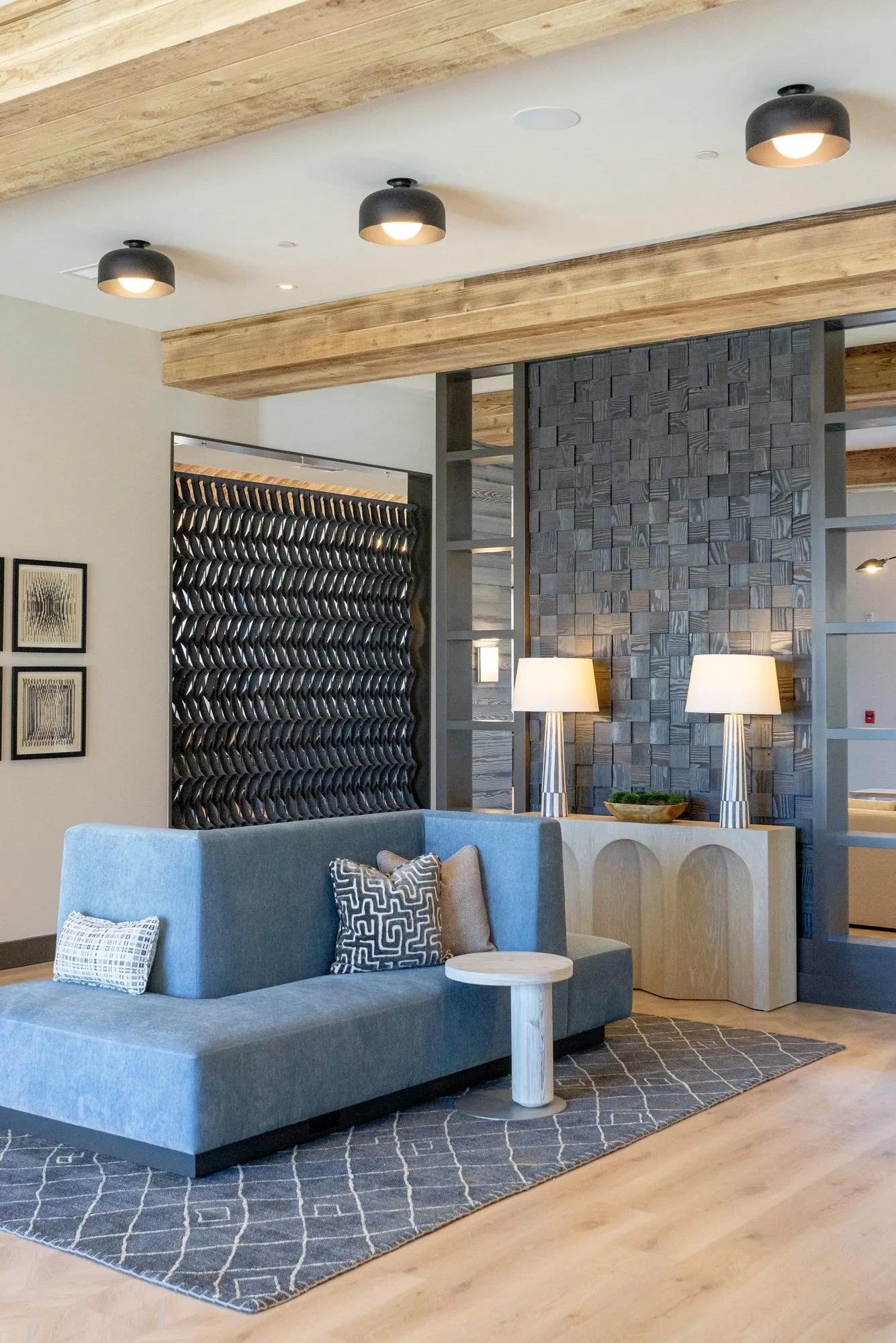 Multifamily interior detail: blue settee and arched console beneath a timber beam, carved block wall and woven panel behind