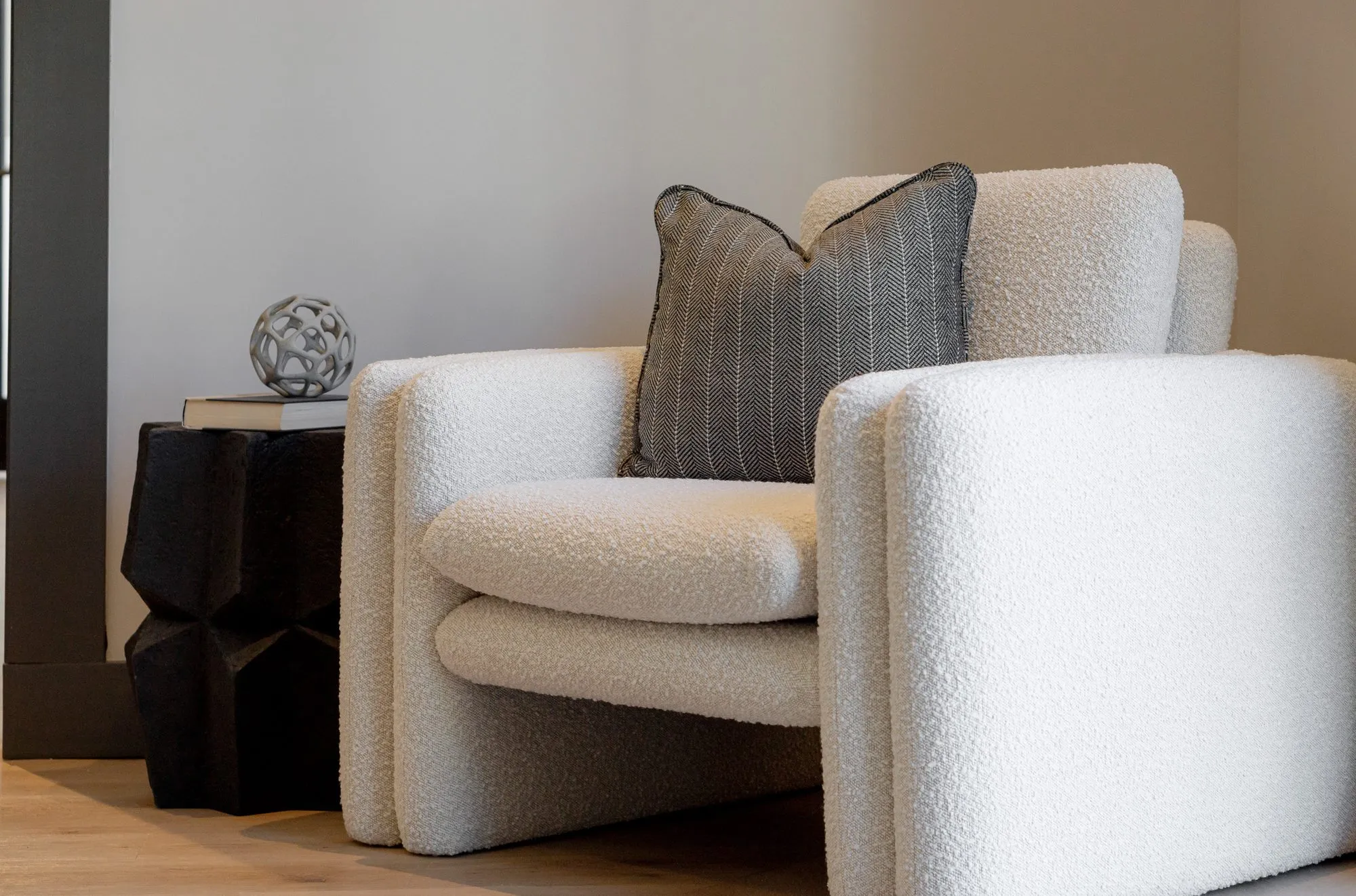 Multifamily interior detail: cream boucle armchair with a striped pillow beside a black faceted side table with a wire sphere