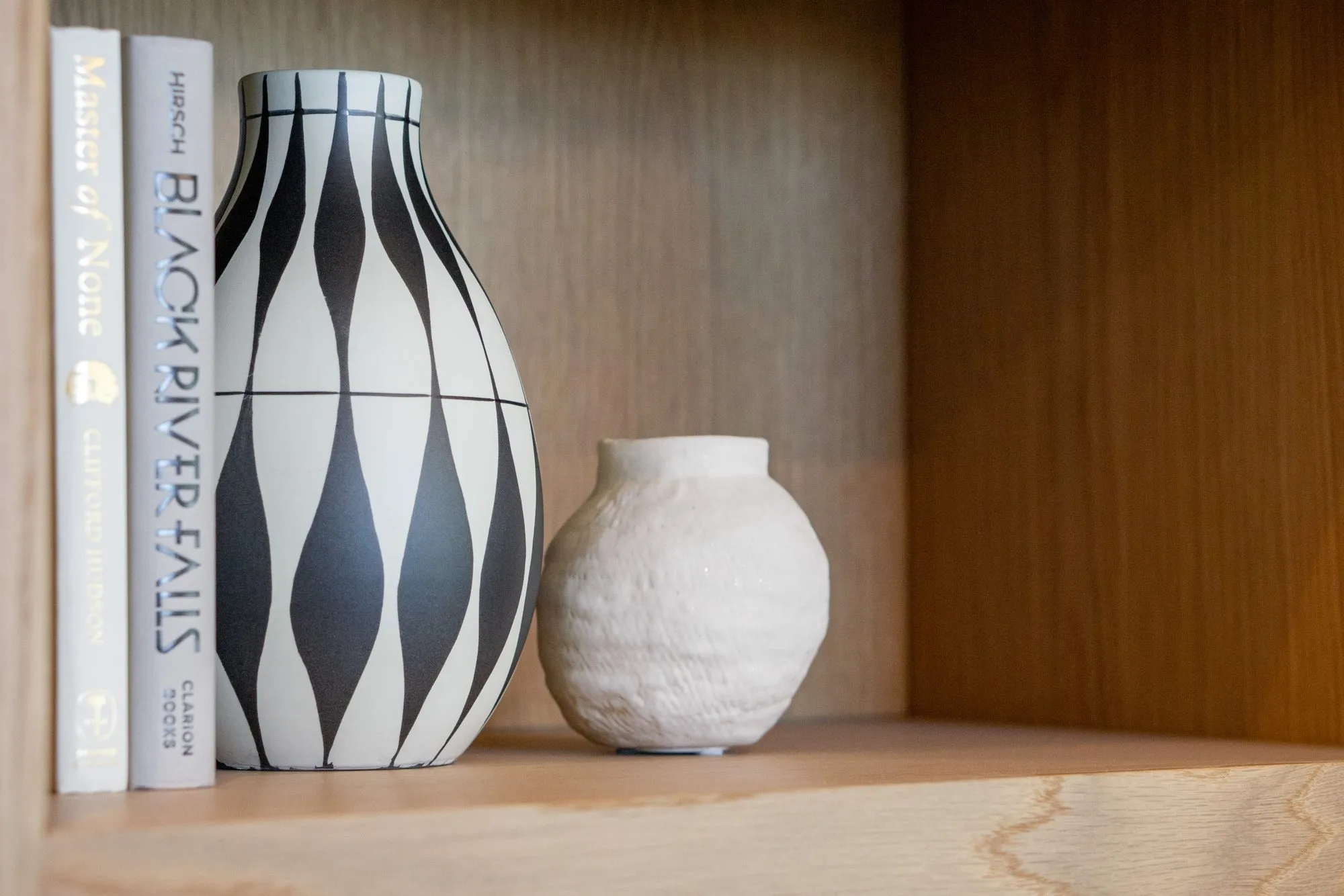 Multifamily interior detail: harlequin vase and white textured pot on an oak shelf beside two books