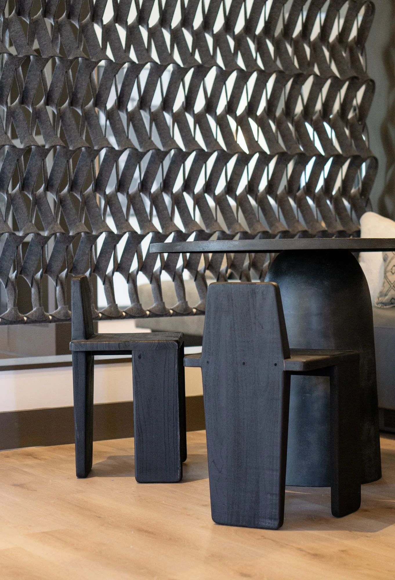 Multifamily interior detail: black wood chairs at a dark pedestal table before a black sculptural acoustic panel