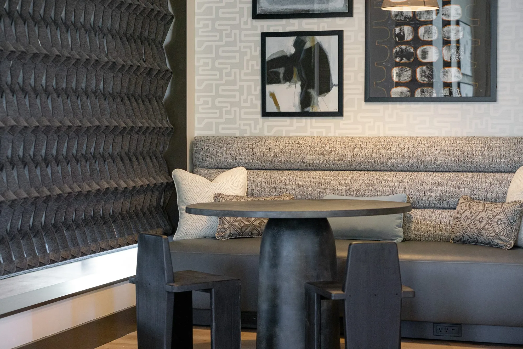 Multifamily amenity banquette nook, a grey bench and black pedestal table between a sculptural black wall and maze wallpaper