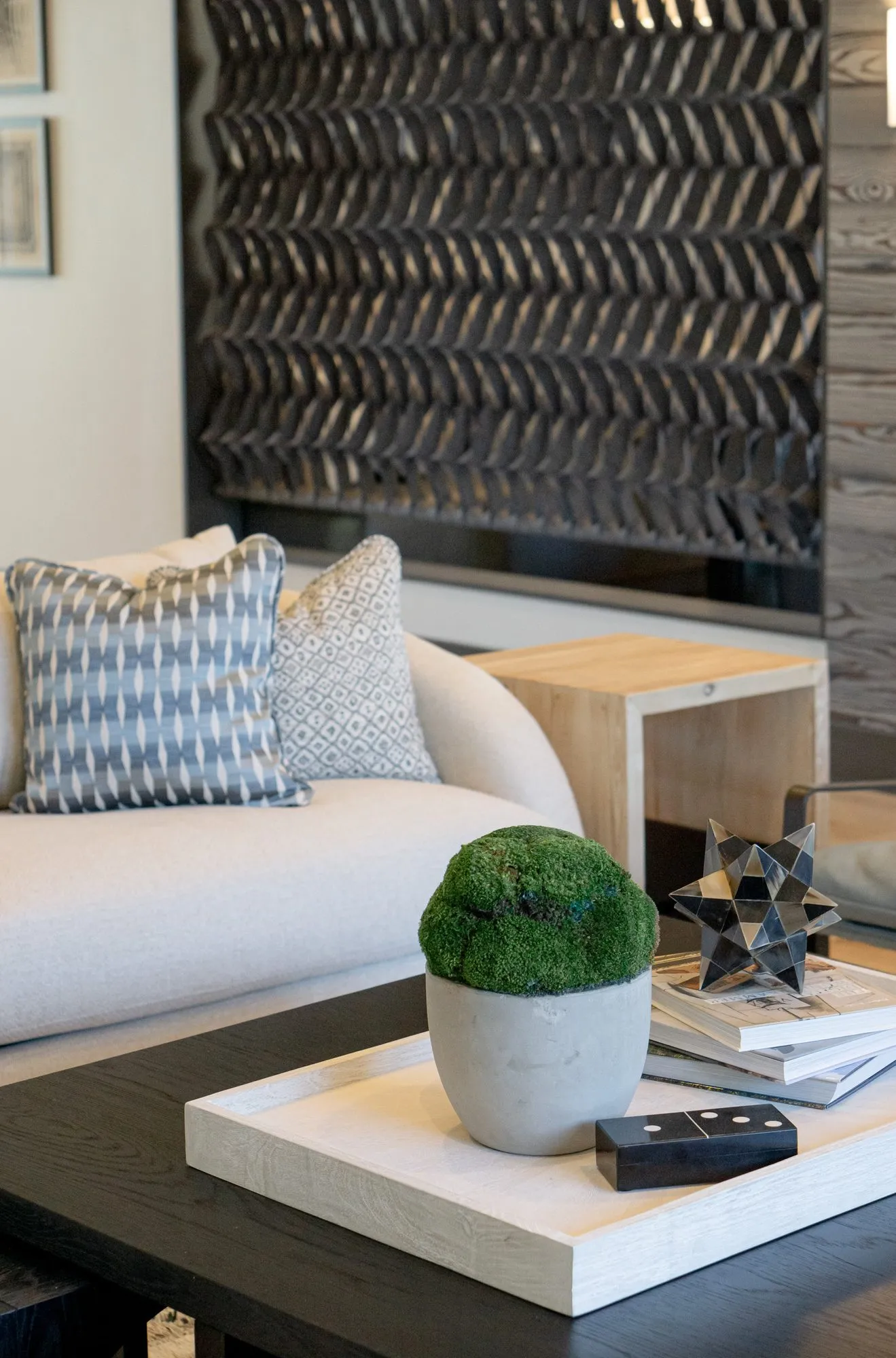 Multifamily interior detail: moss pot and star sculpture on a white tray, cream sofa and black chevron panel behind