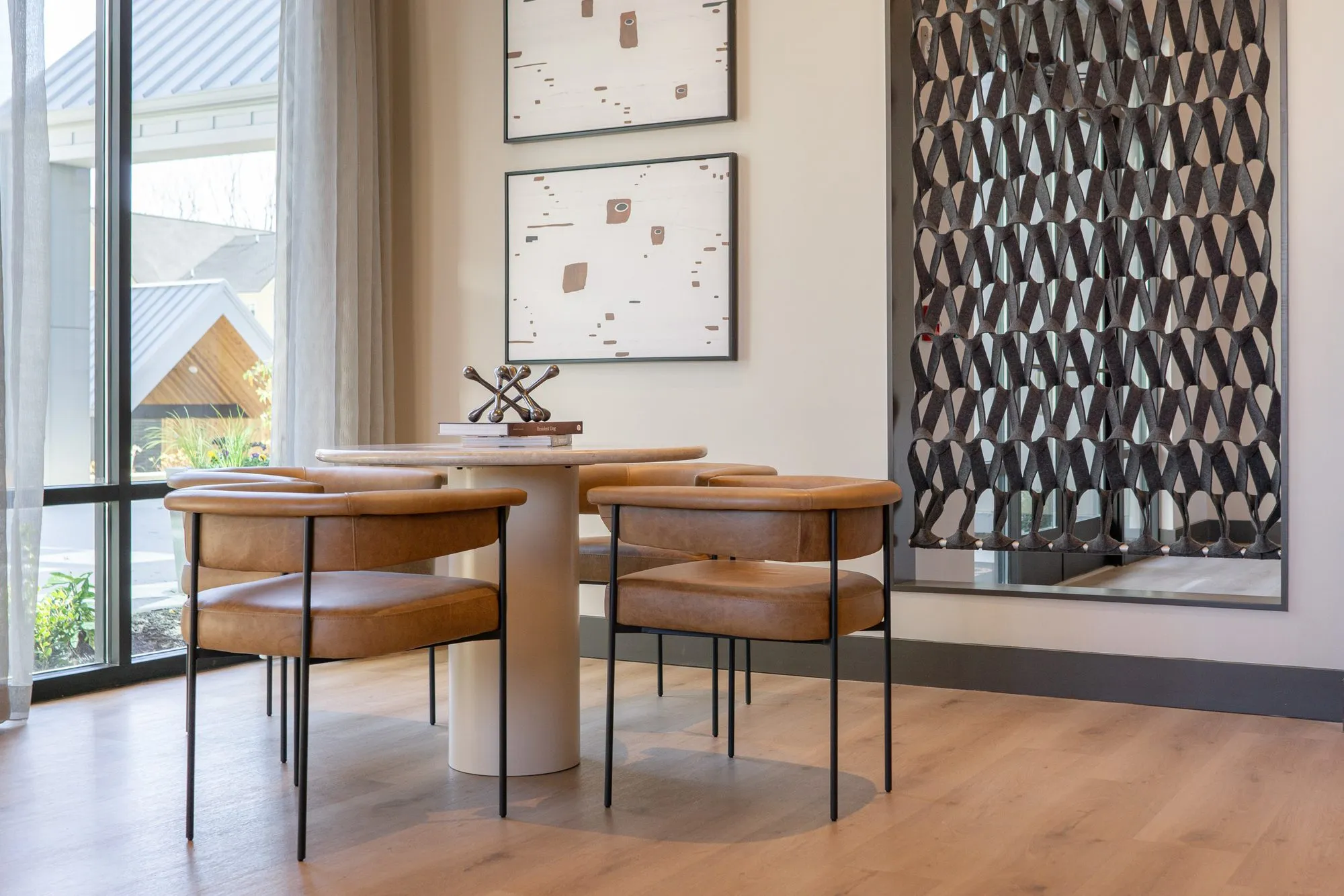 Multifamily dining nook with tan leather chairs at a white pedestal table by floor to ceiling windows, two prints above