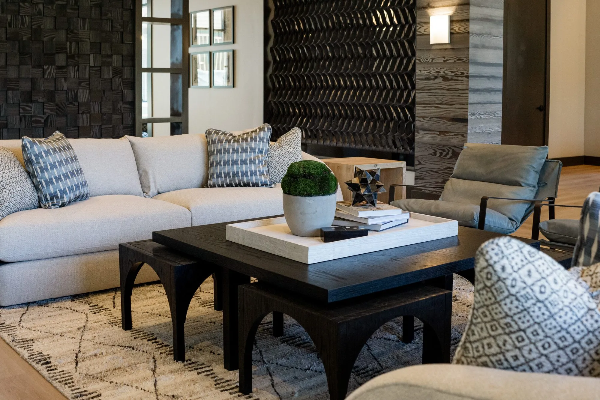 Multifamily amenity lounge with a cream sofa and black arched-leg coffee tables on a diamond rug, carved block walls behind