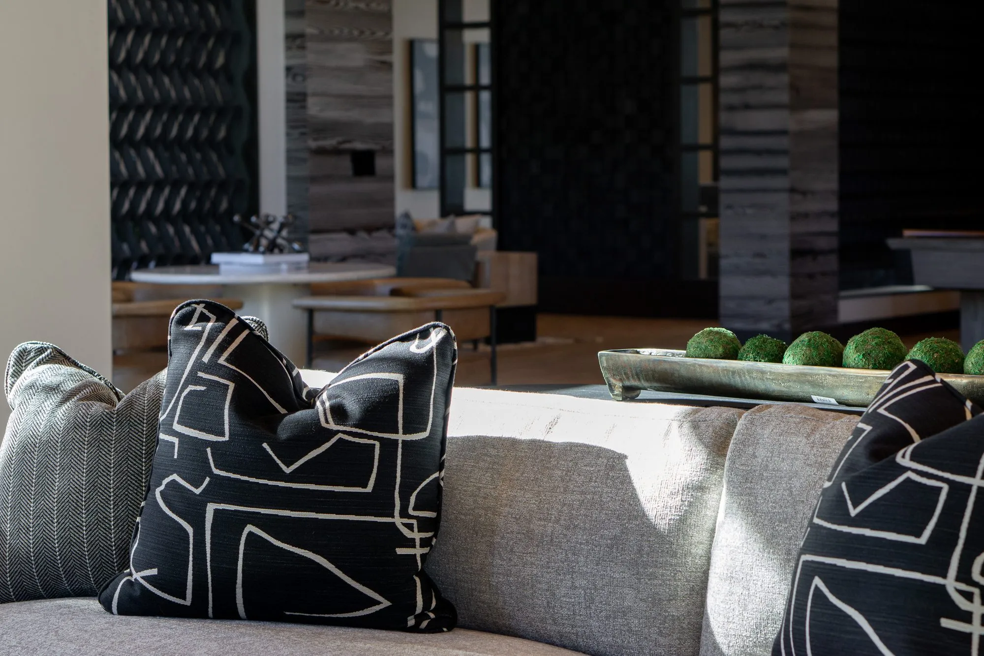 Multifamily interior detail: black and white graphic pillows on a grey sofa, moss balls on a wood tray, the lounge behind