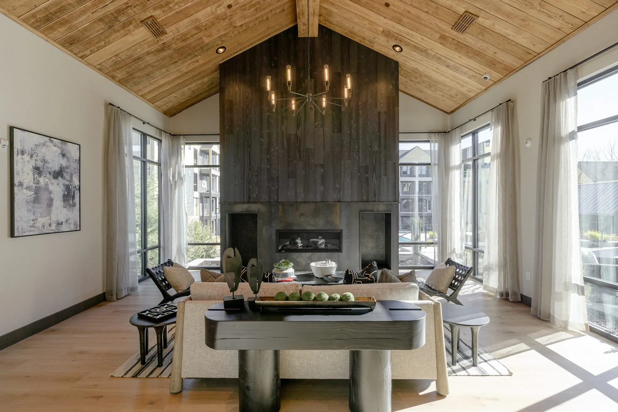 Multifamily amenity clubroom with a charred wood chimney and linear fireplace under a plank vault, a console behind the sofa