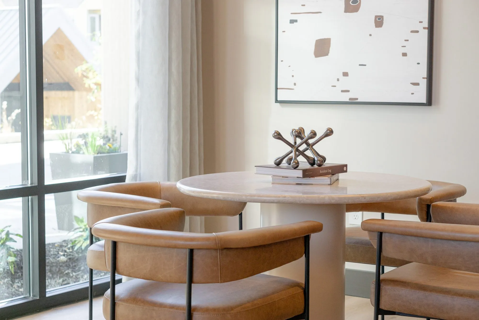 Multifamily interior detail: tan leather chairs around the round stone table, a jack sculpture on books, garden beyond