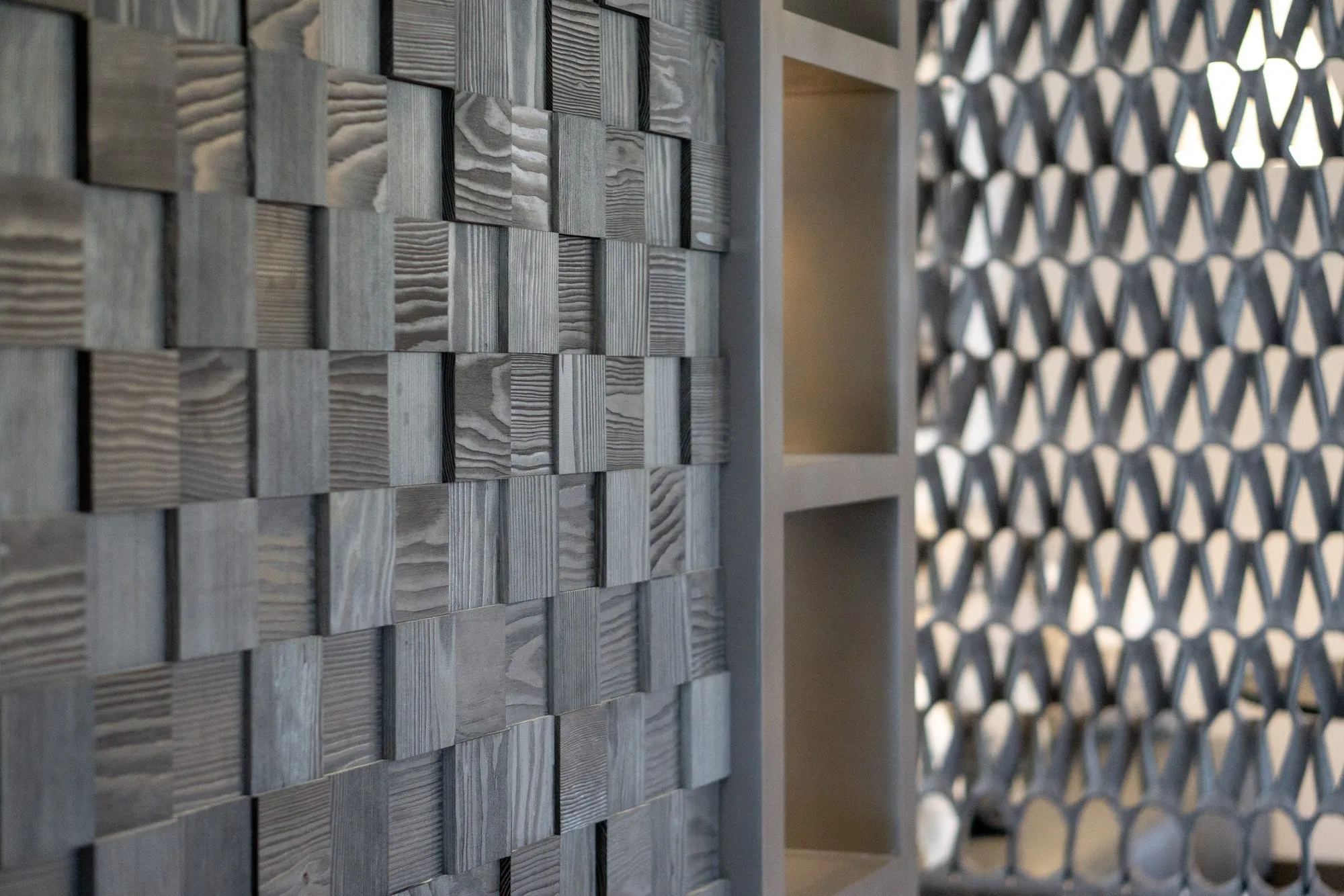 Multifamily interior detail: grey wood block wall beside oak shelving and a black chevron screen