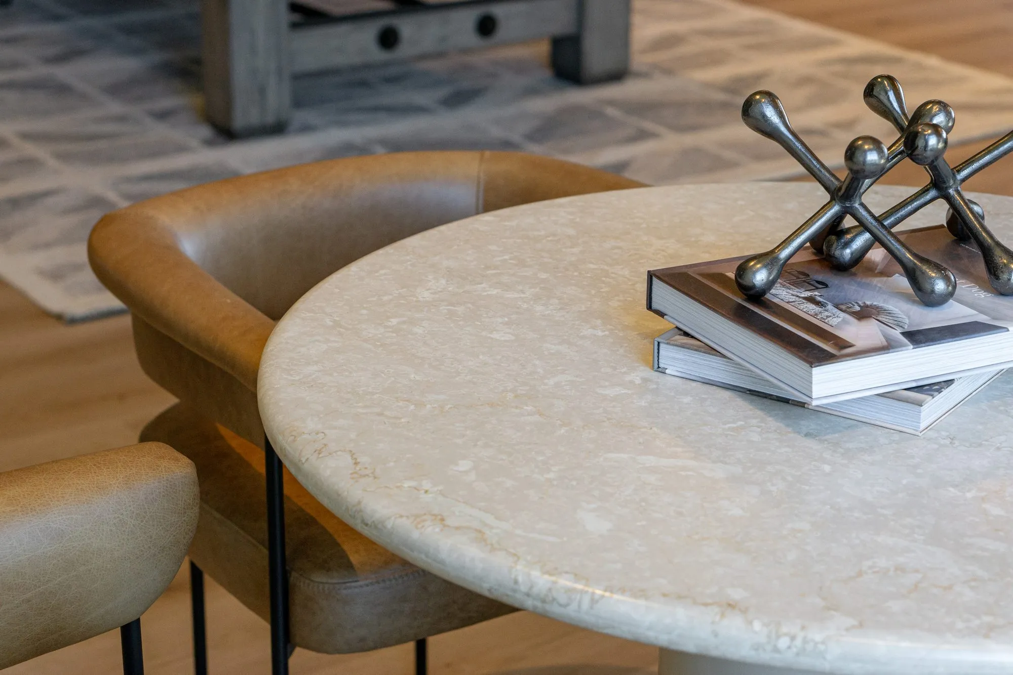 Multifamily interior detail: jack sculpture on books atop a round stone table beside a tan leather chair