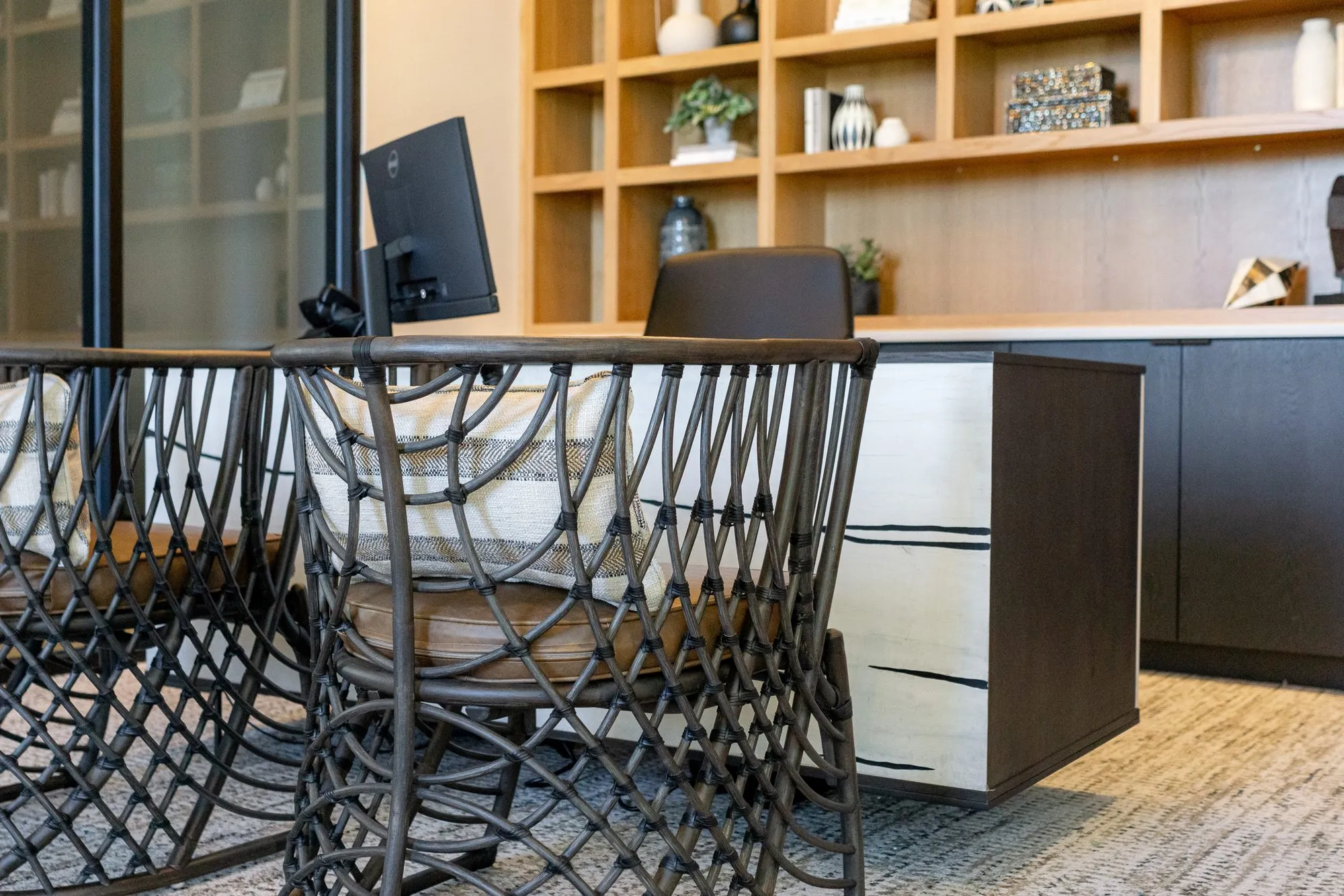 Multifamily amenity leasing desk detail: woven black chairs, a monitor and oak shelving behind