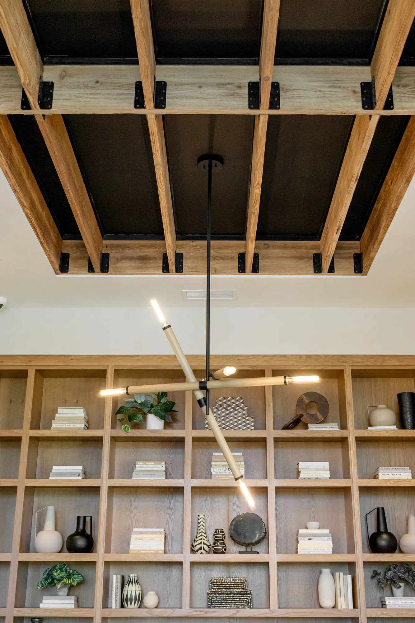 Multifamily interior detail: linear brass and glass pendant below exposed timber joists before oak shelving with ceramics
