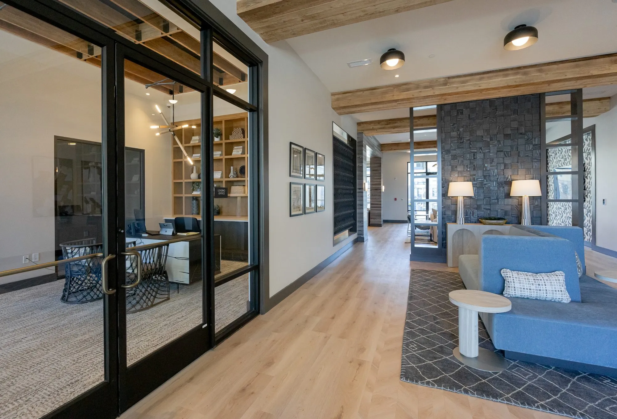 Multifamily amenity corridor with glass doors to the leasing office at left and the blue settee lounge at right