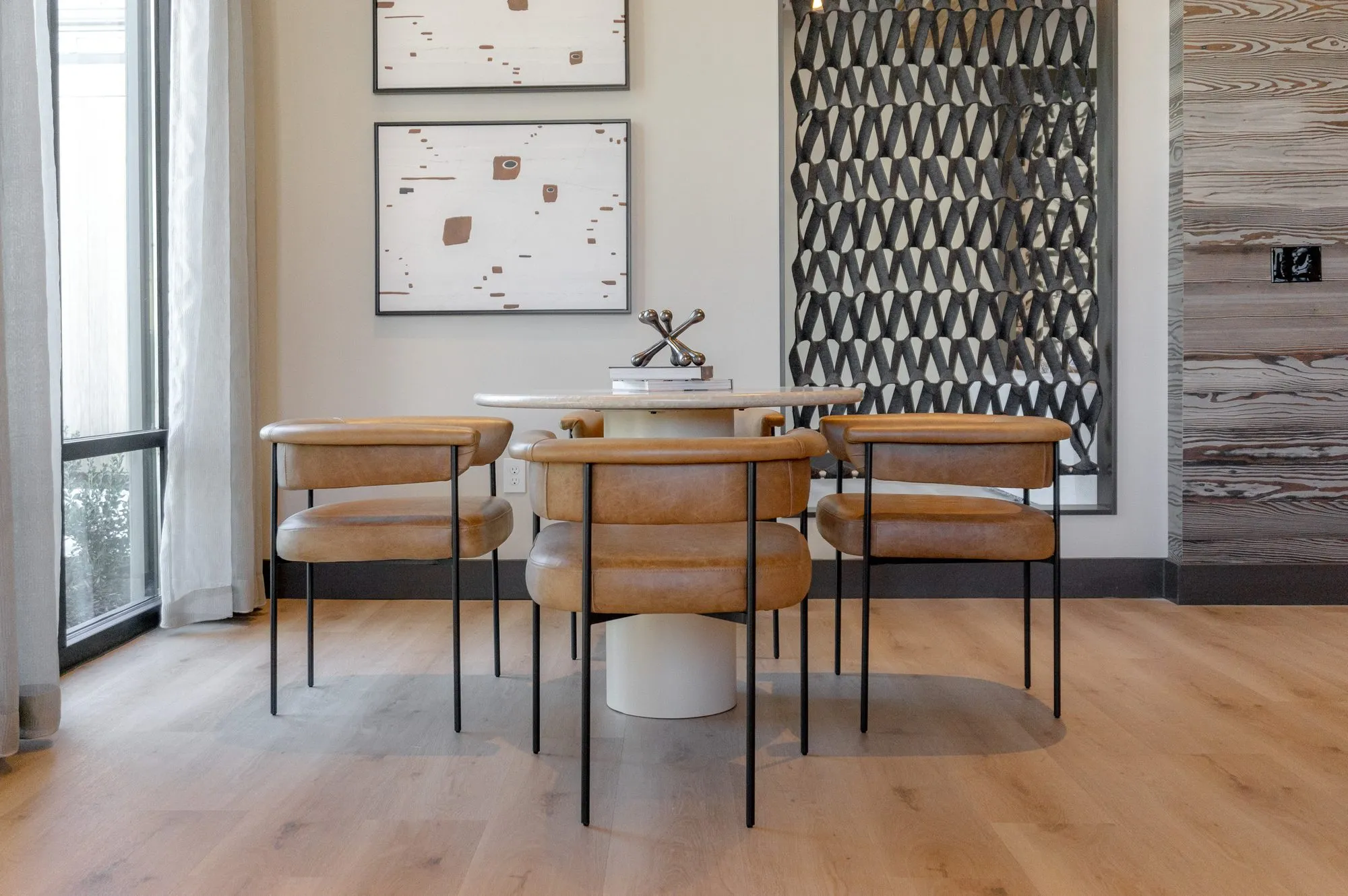 Multifamily dining nook with tan leather chairs at a pedestal table between a black patterned screen and curtained window