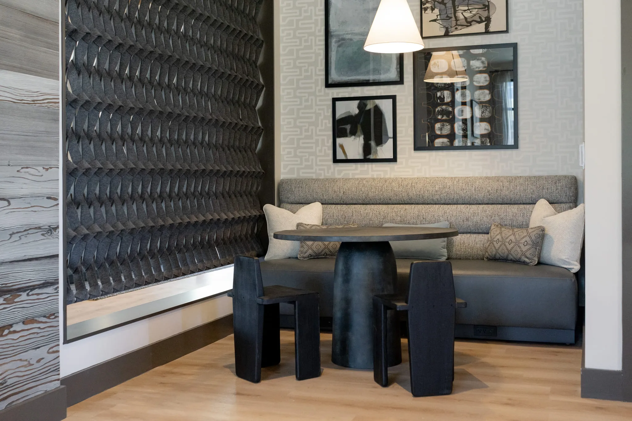 Multifamily banquette nook with an upholstered bench, a black pedestal table and chairs against a sculptural tile wall