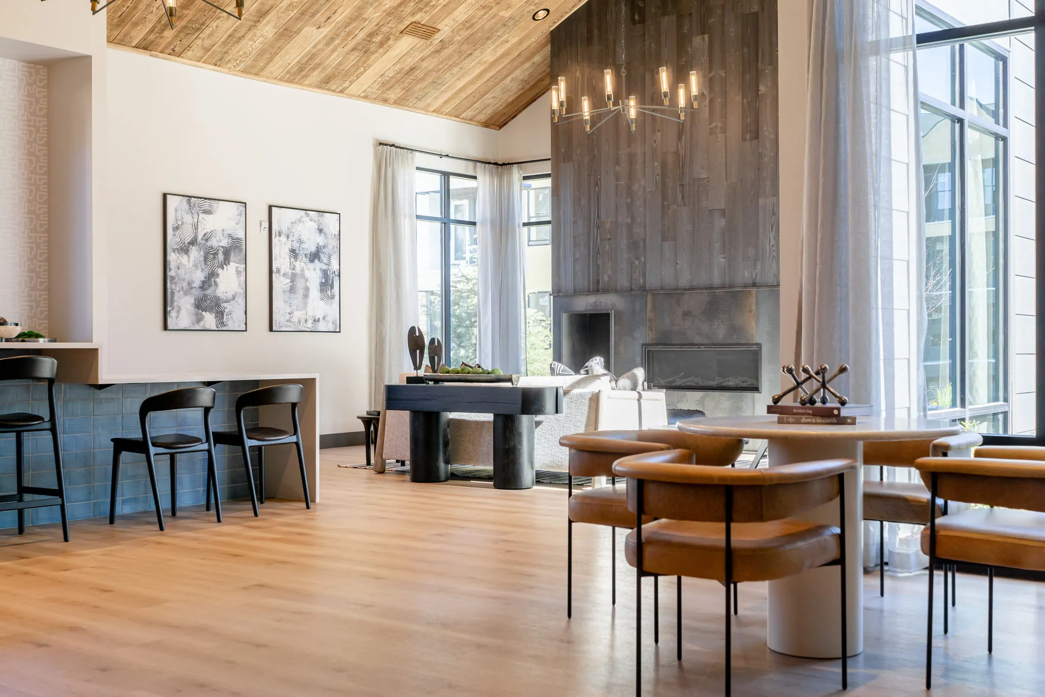 Multifamily amenity clubroom with a vaulted wood ceiling above a round table with tan leather chairs and wood-clad fireplace