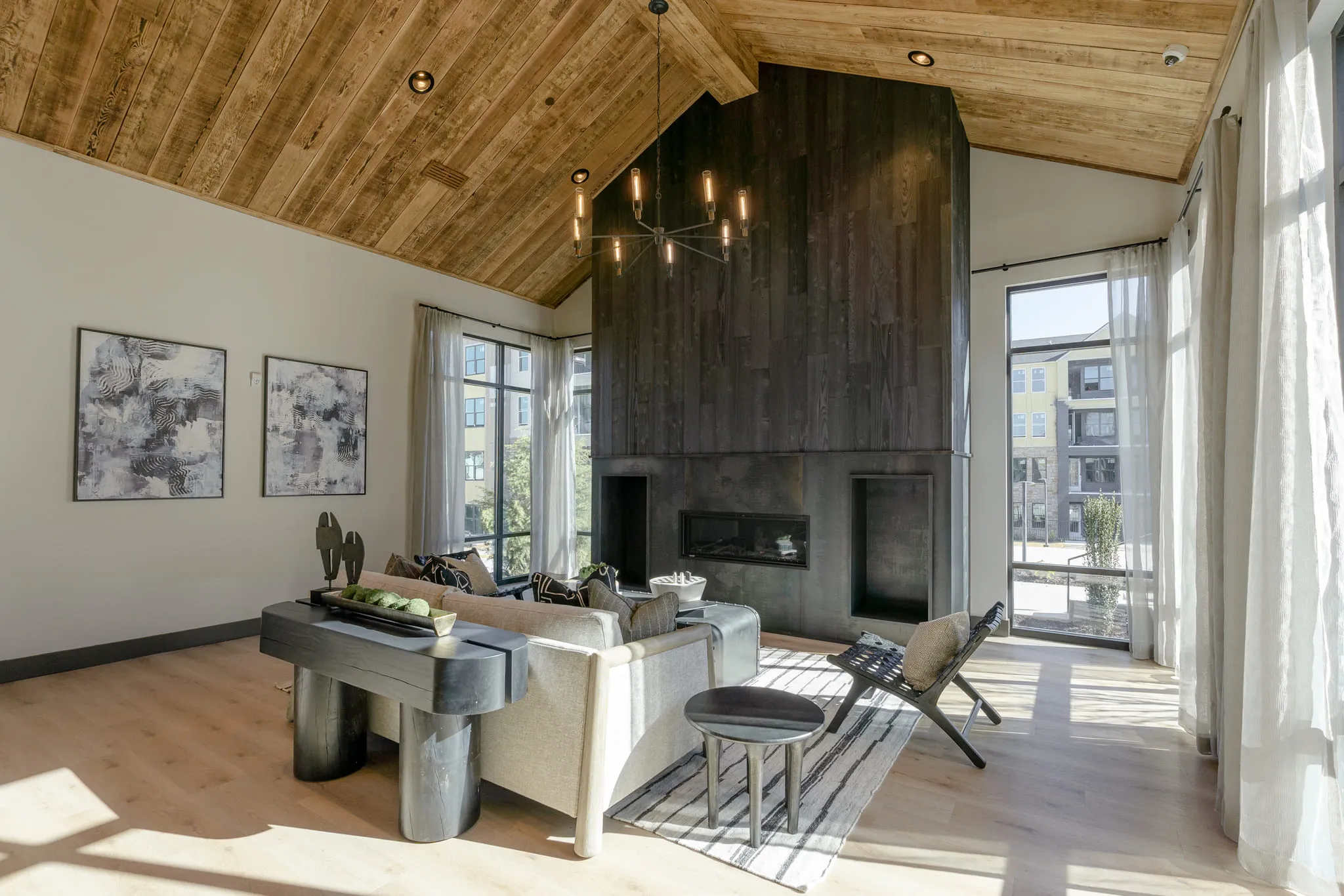 Multifamily amenity clubroom from an angle, charred wood chimney and linear fireplace, abstract prints and curtained windows