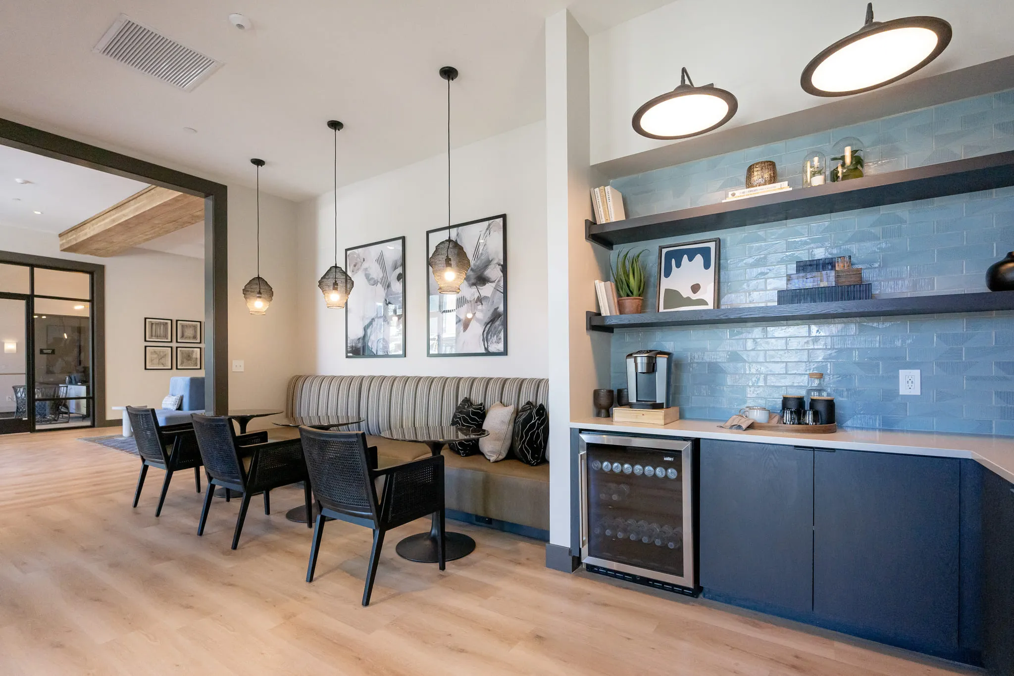 Multifamily amenity coffee bar with a blue tile wall and open shelving beside a striped banquette with black cafe chairs