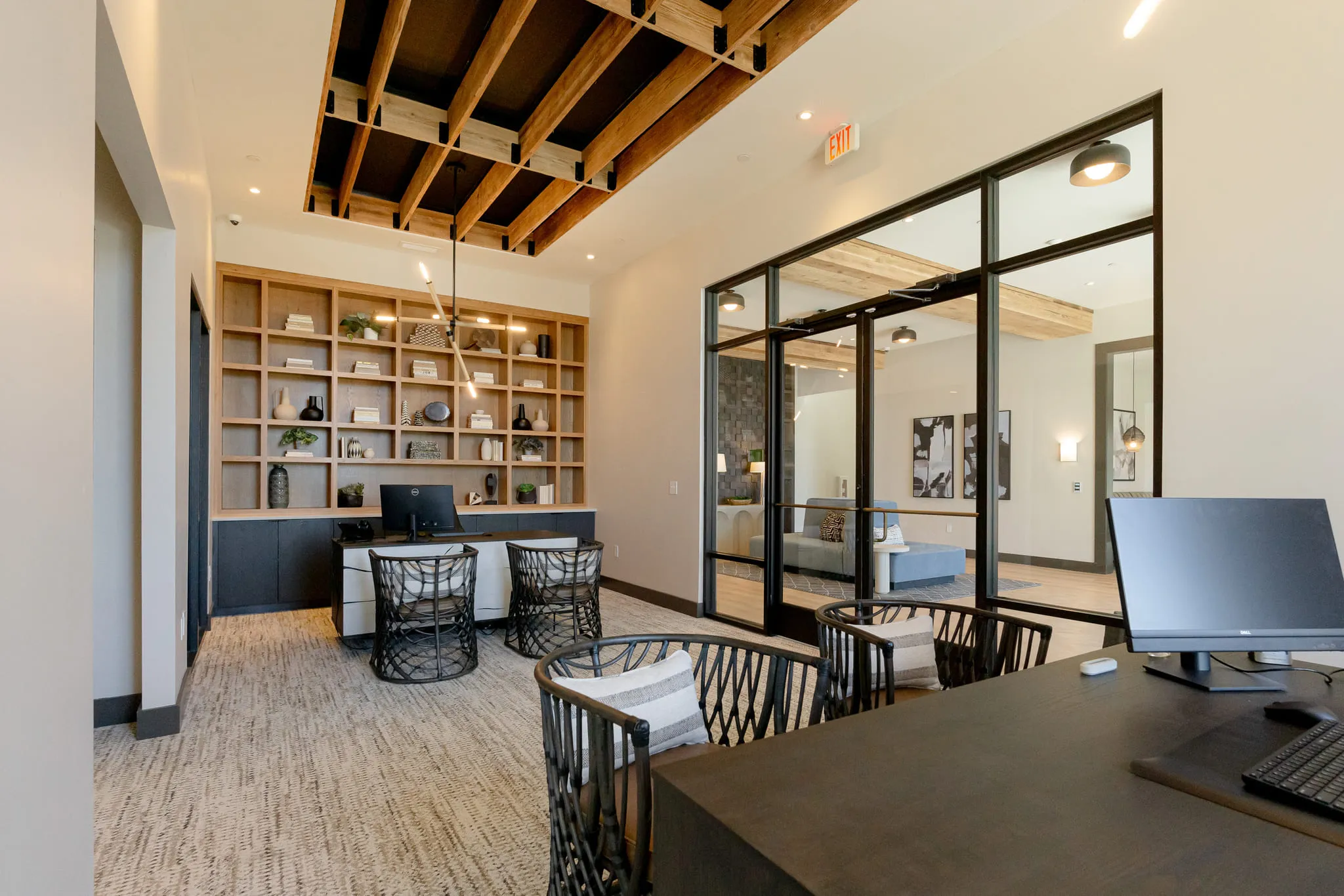 Multifamily amenity coworking library with oak shelving and glass-walled offices below exposed timber trusses