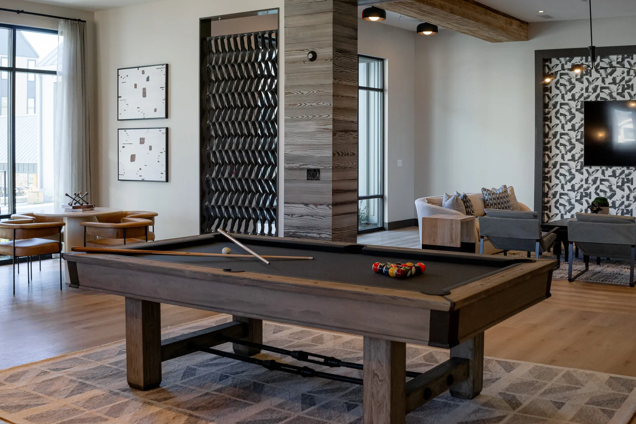 Multifamily amenity game room with a pool table under a timber beam beside patterned screen partitions