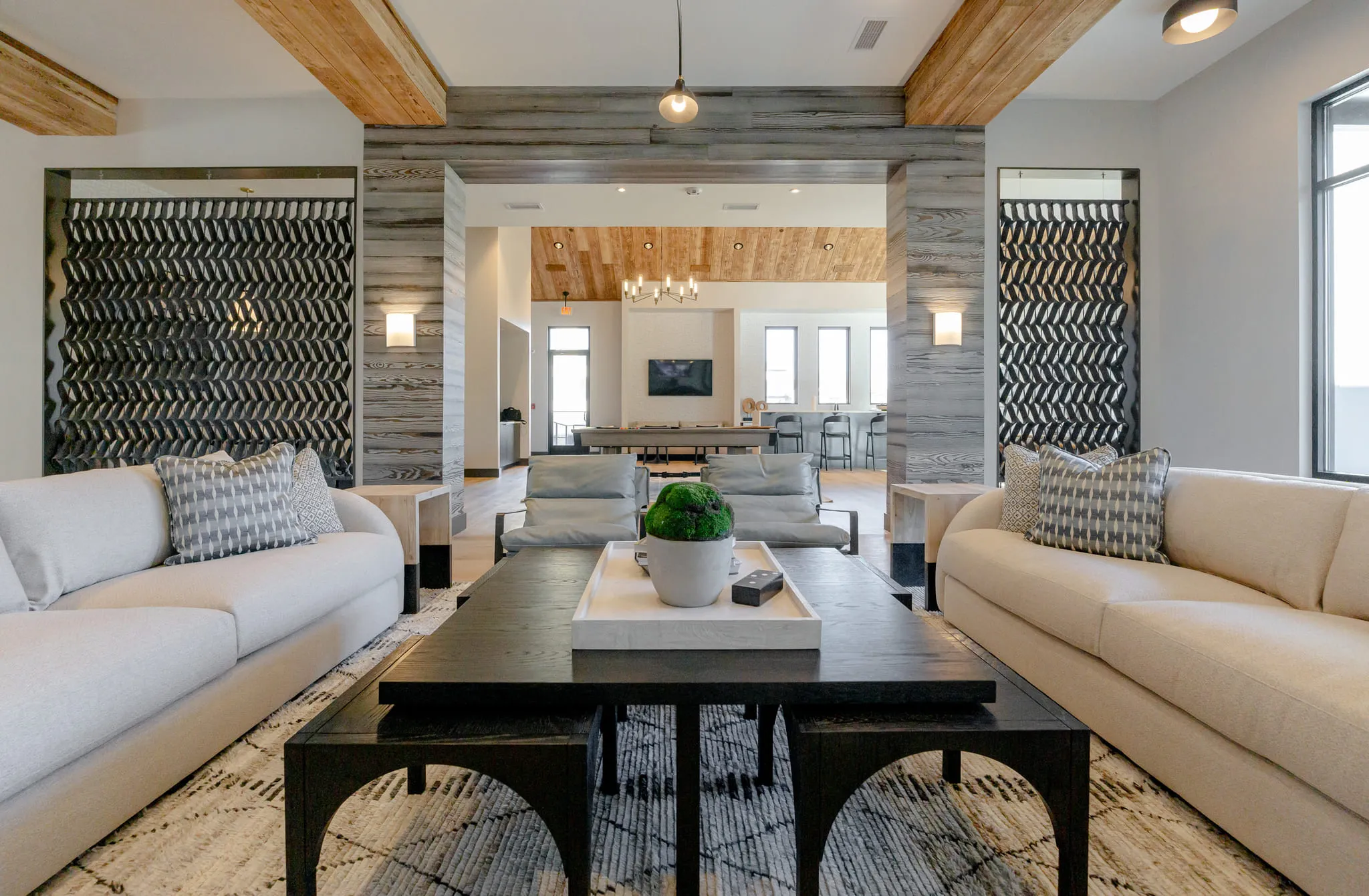 Multifamily amenity lounge with two facing cream sofas and a dark coffee table framed by textural acoustic screens