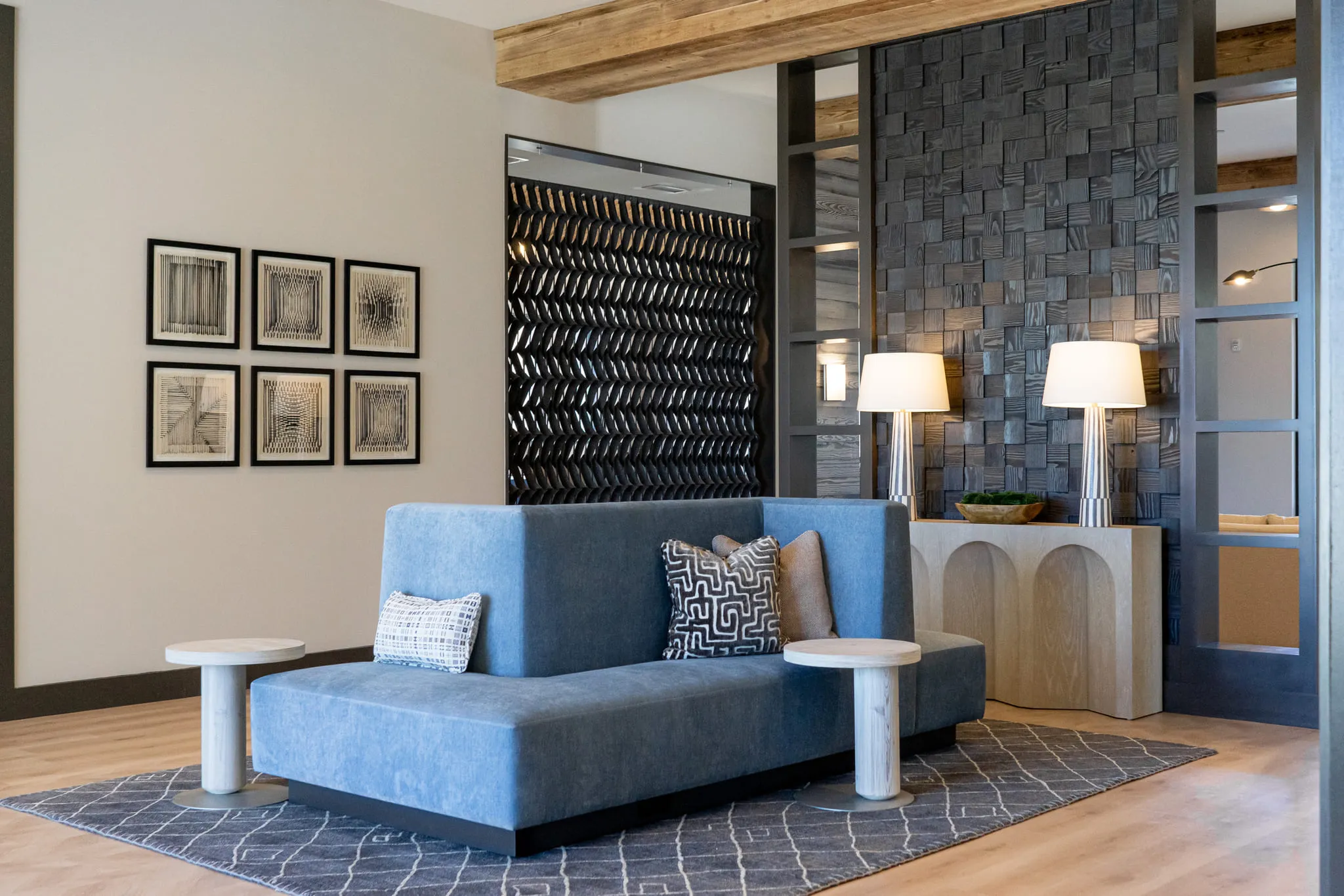 Multifamily seating area with a blue sofa before an arched plaster console and lamps, a grid of framed prints at left