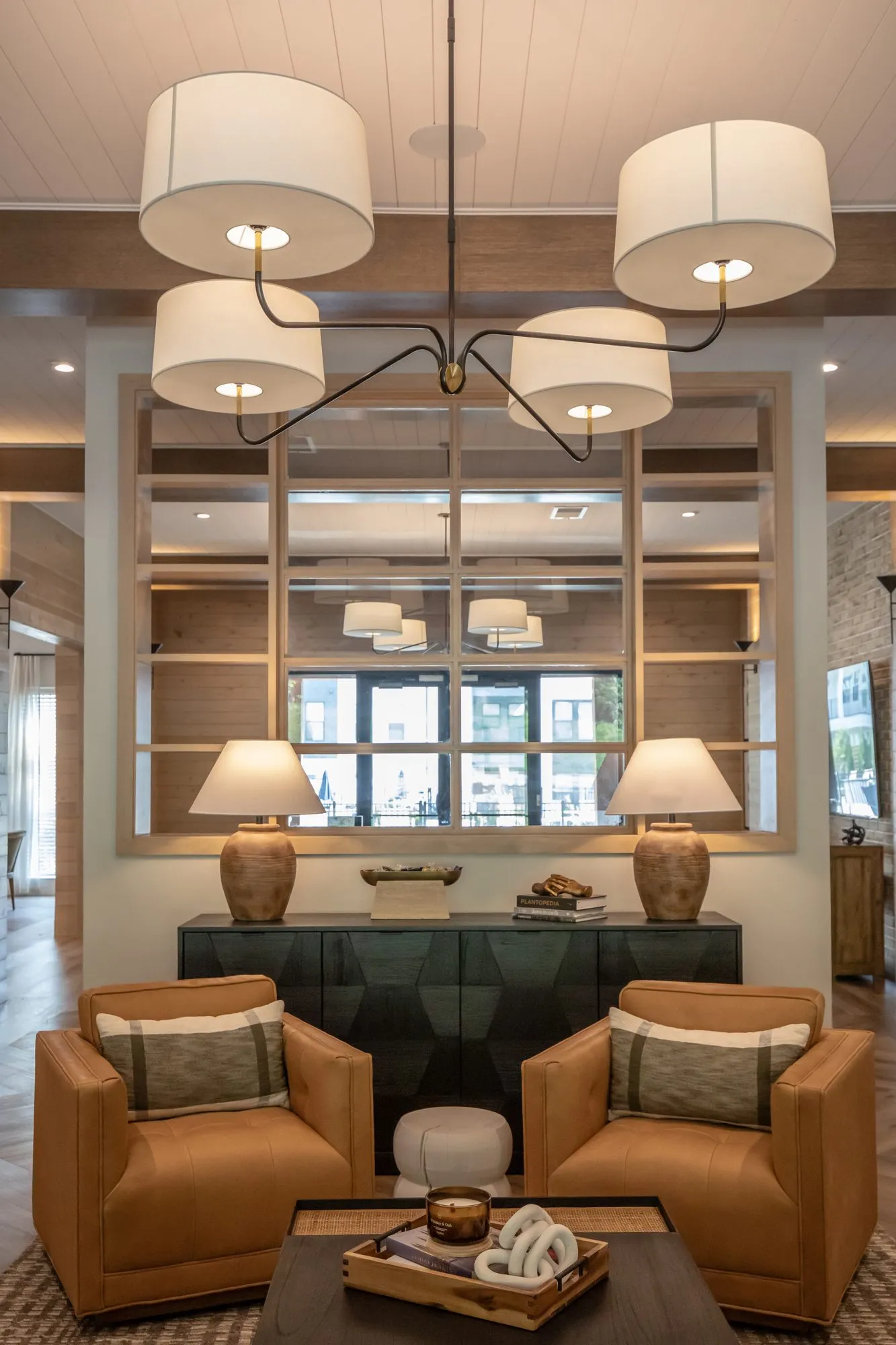 Multifamily interior detail: tan leather armchairs before a dark console with ceramic lamps under a four shade chandelier