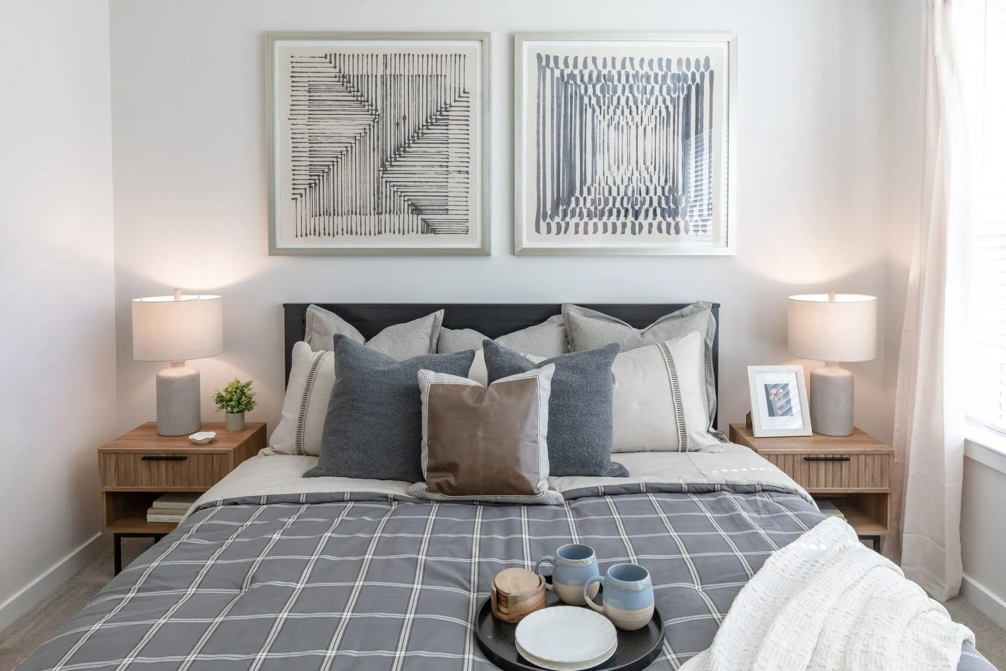 Multifamily model apartment bedroom with a plaid duvet, rattan nightstands and two framed geometric prints