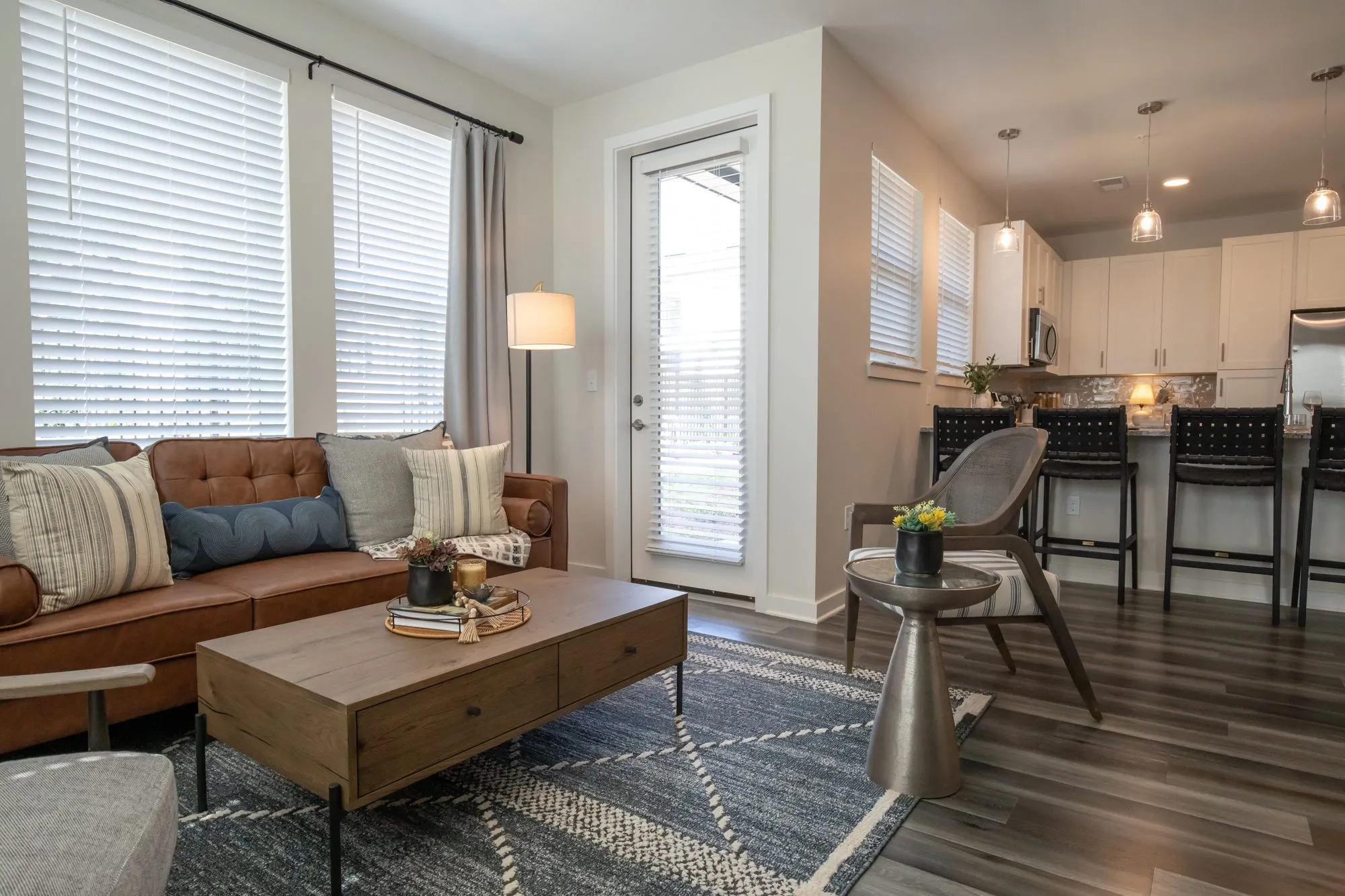 Multifamily model apartment living room with a cognac leather sofa and wood coffee table, open to a kitchen with barstools