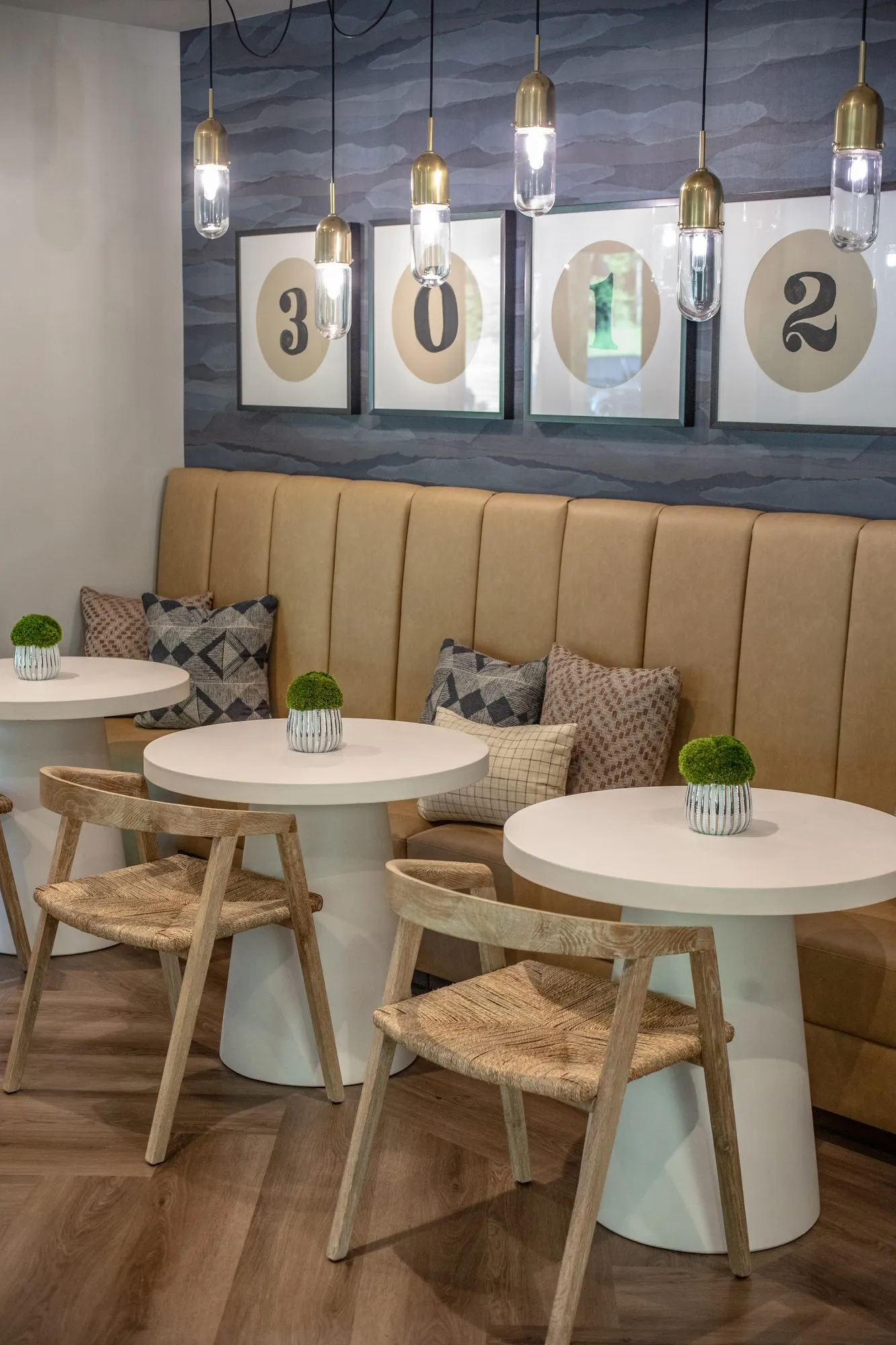 Multifamily interior detail: tan banquette, round white pedestal tables and rush seat chairs below numbered prints